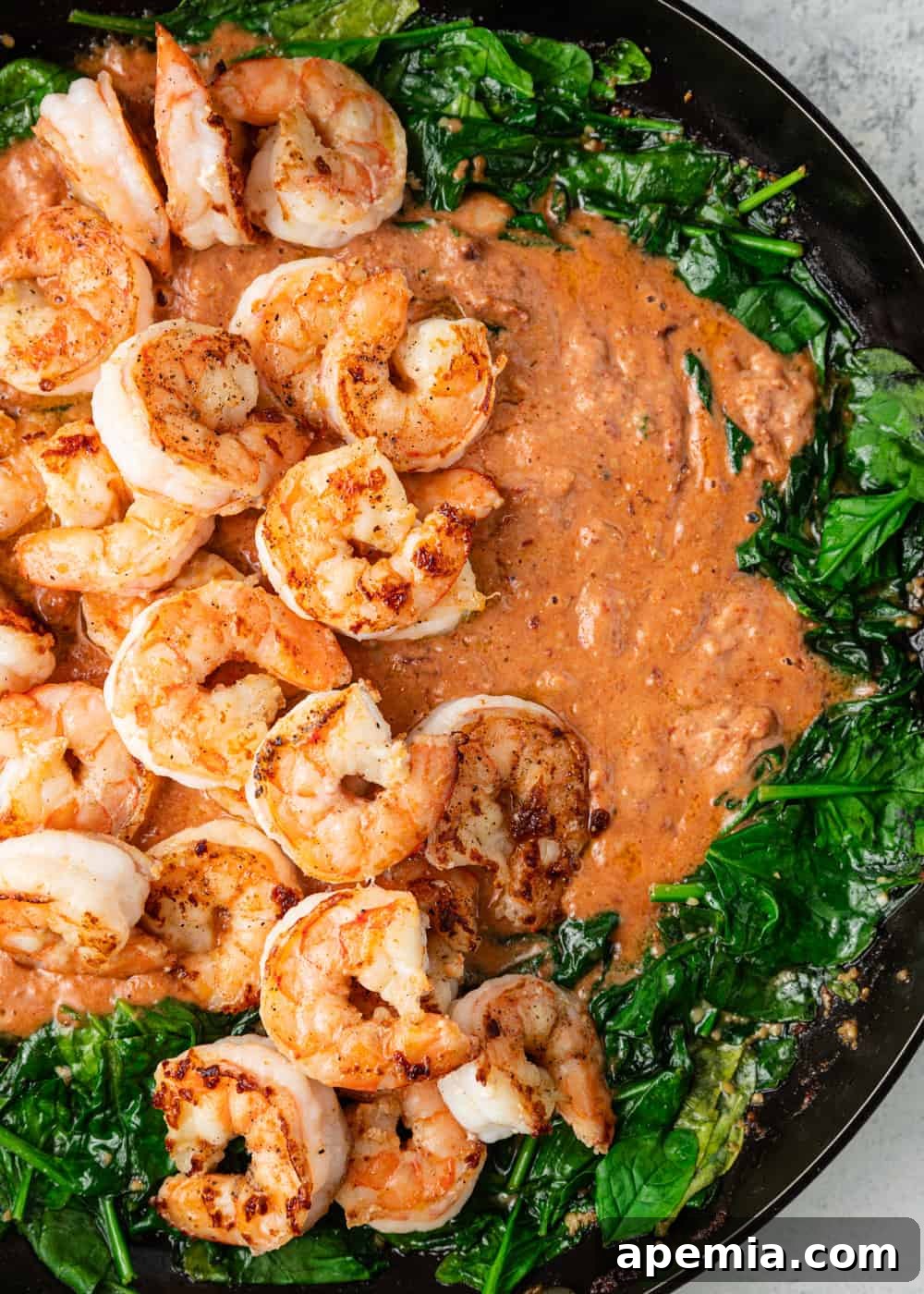Overhead closeup of Tuscan shrimp actively cooking in a creamy sauce with vibrant spinach, showing the rich texture.