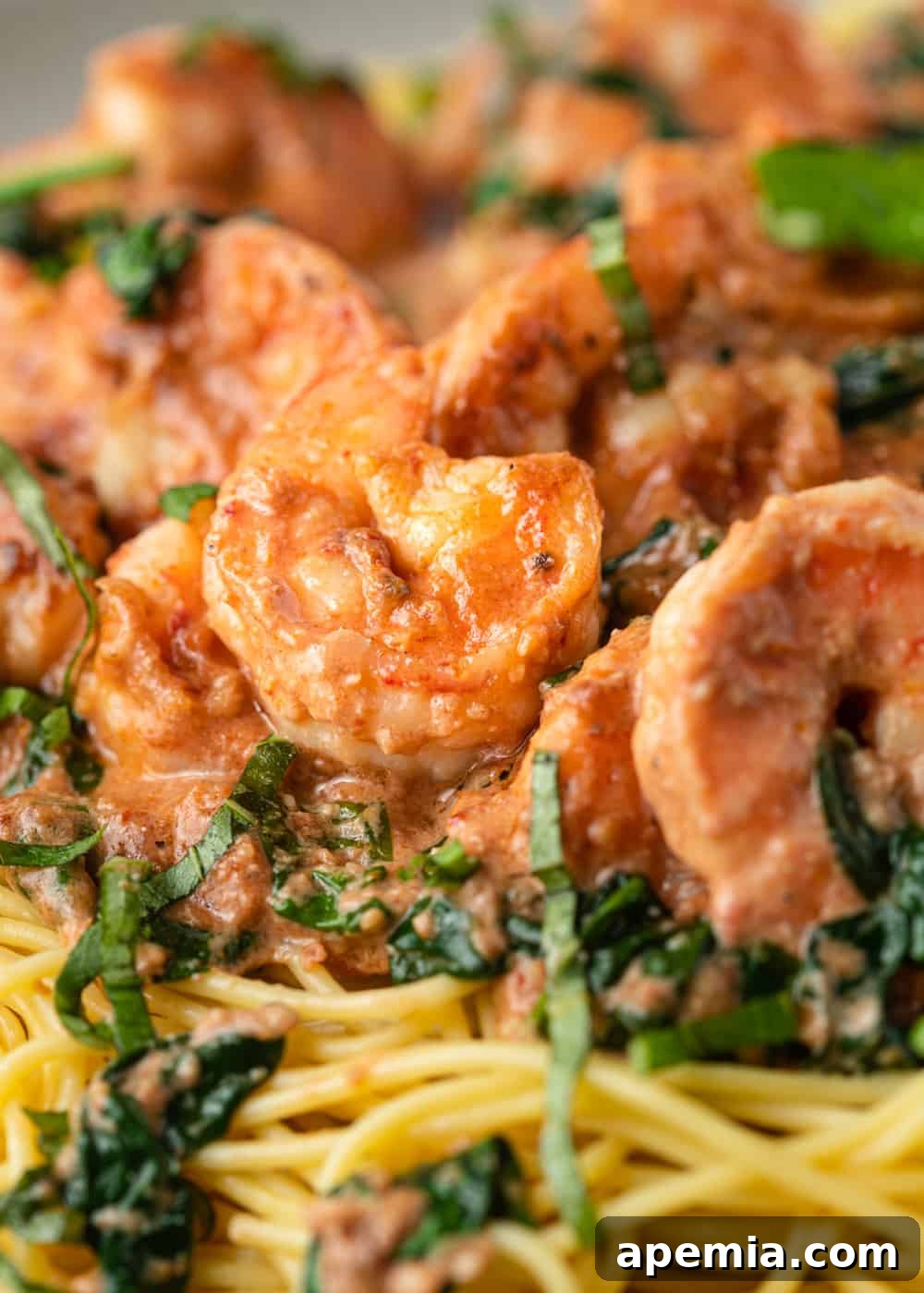 Closeup of Tuscan shrimp nestled in a creamy sauce with spinach, perfectly plated over spaghetti for serving.