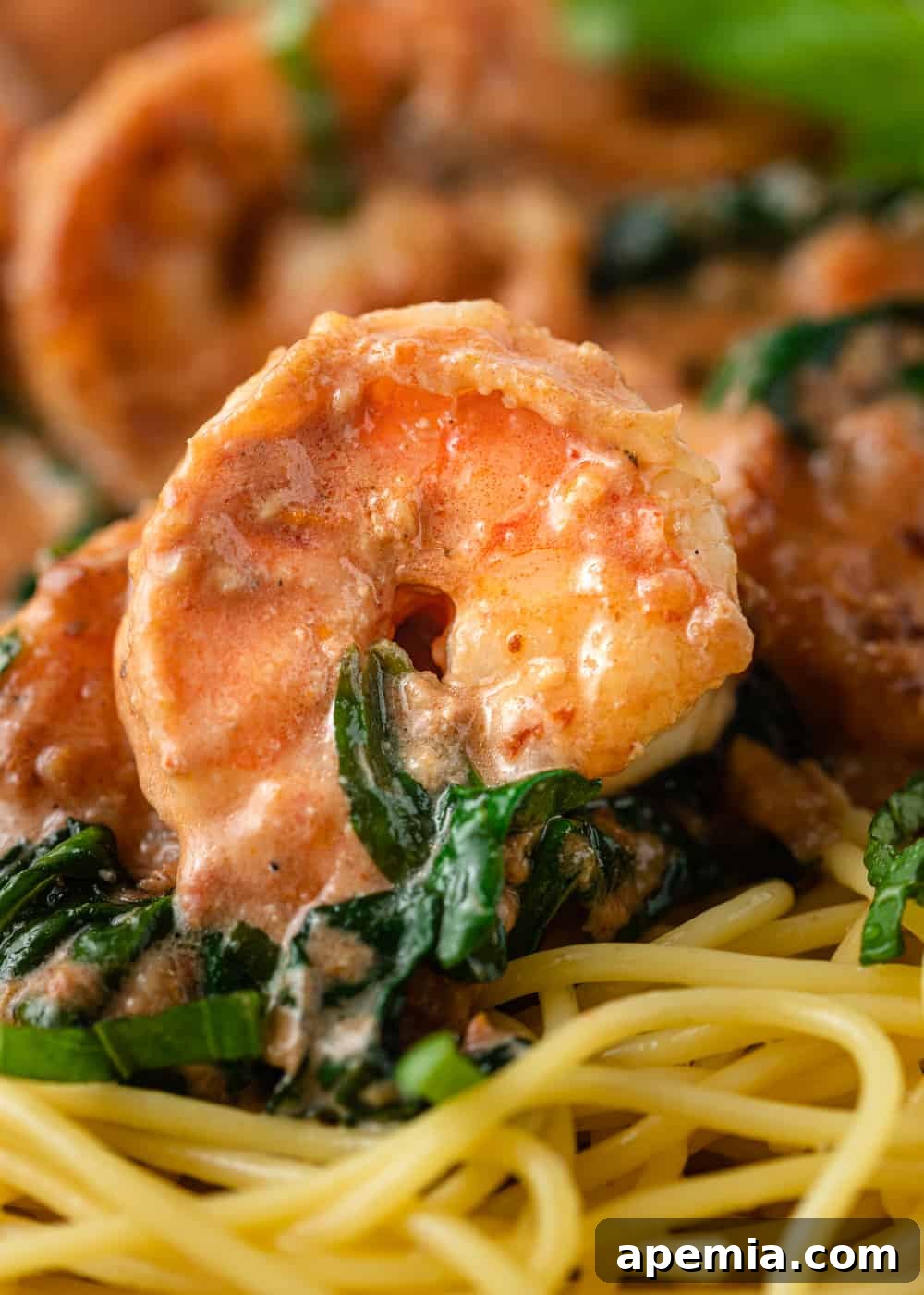 Closeup of several perfectly cooked Tuscan shrimps with spinach, beautifully plated over spaghetti for a satisfying meal.