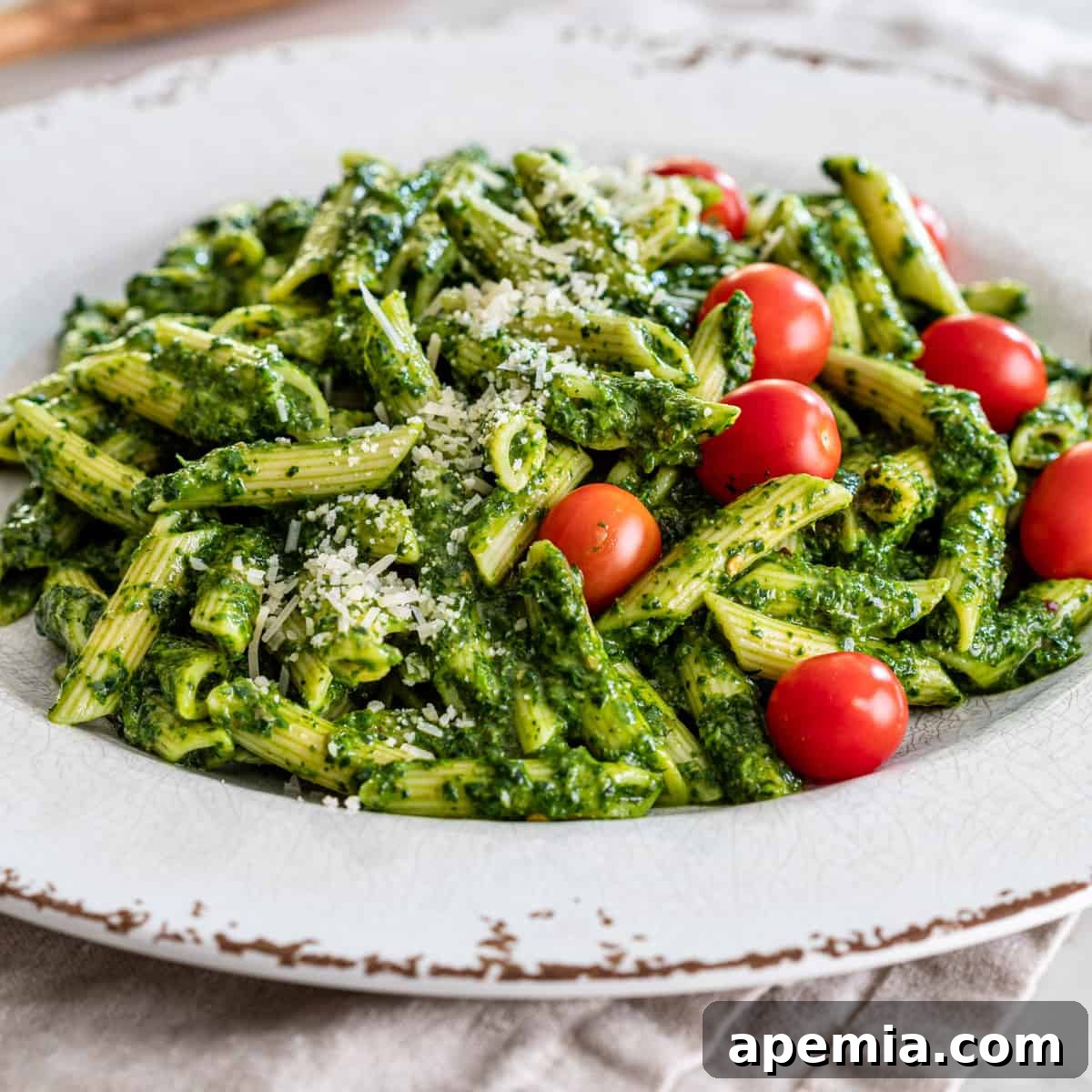 Vibrant Italian Green Sauce 2 closeup side view: a plate of penne pasta with italian salsa verde sauce, parmesan, and whole cherry tomatoes