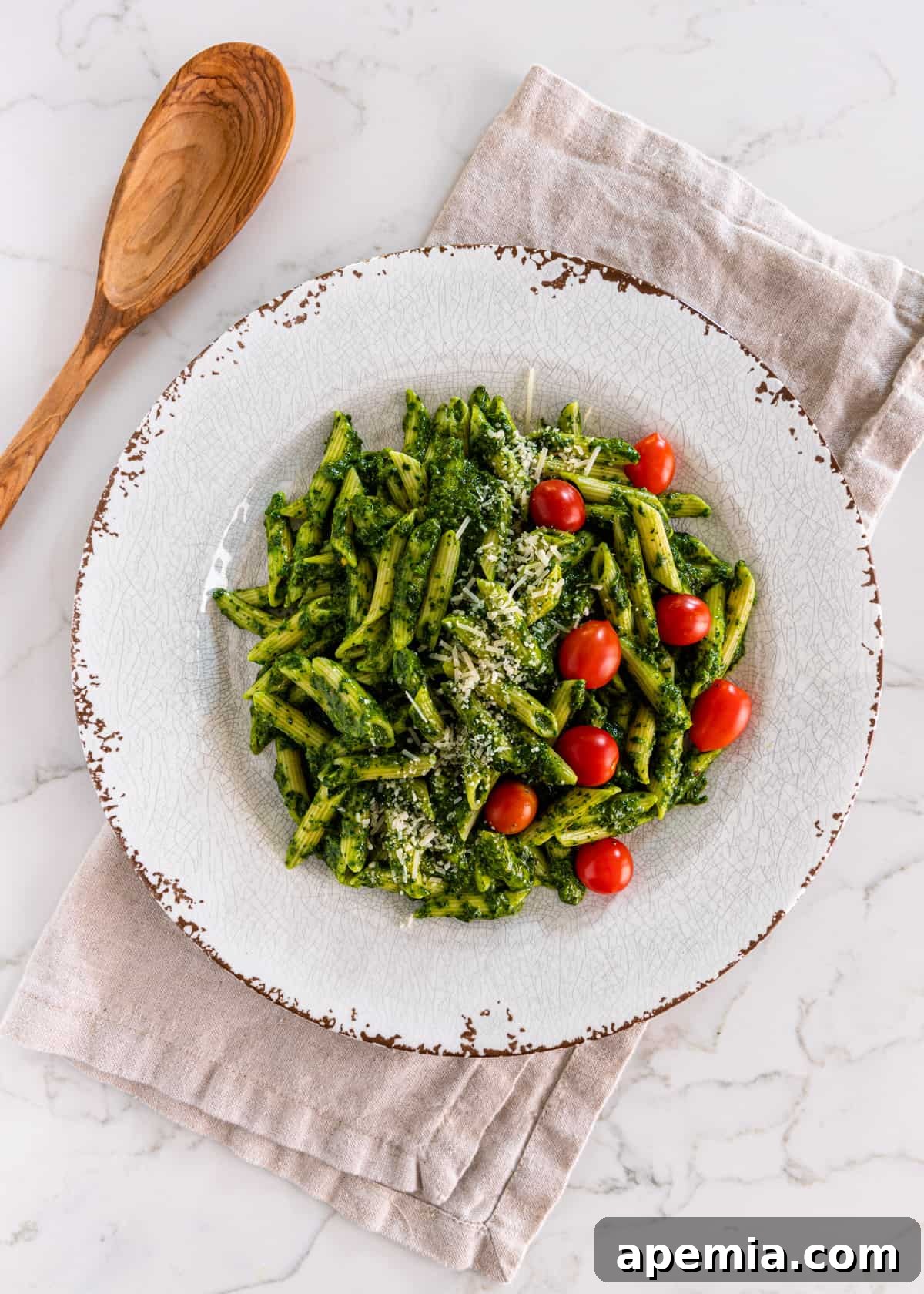 Vibrant Italian Green Sauce 3 overhead: a white plate of penne pasta covered in sauce verde with parmesan and cherry tomatoes on top