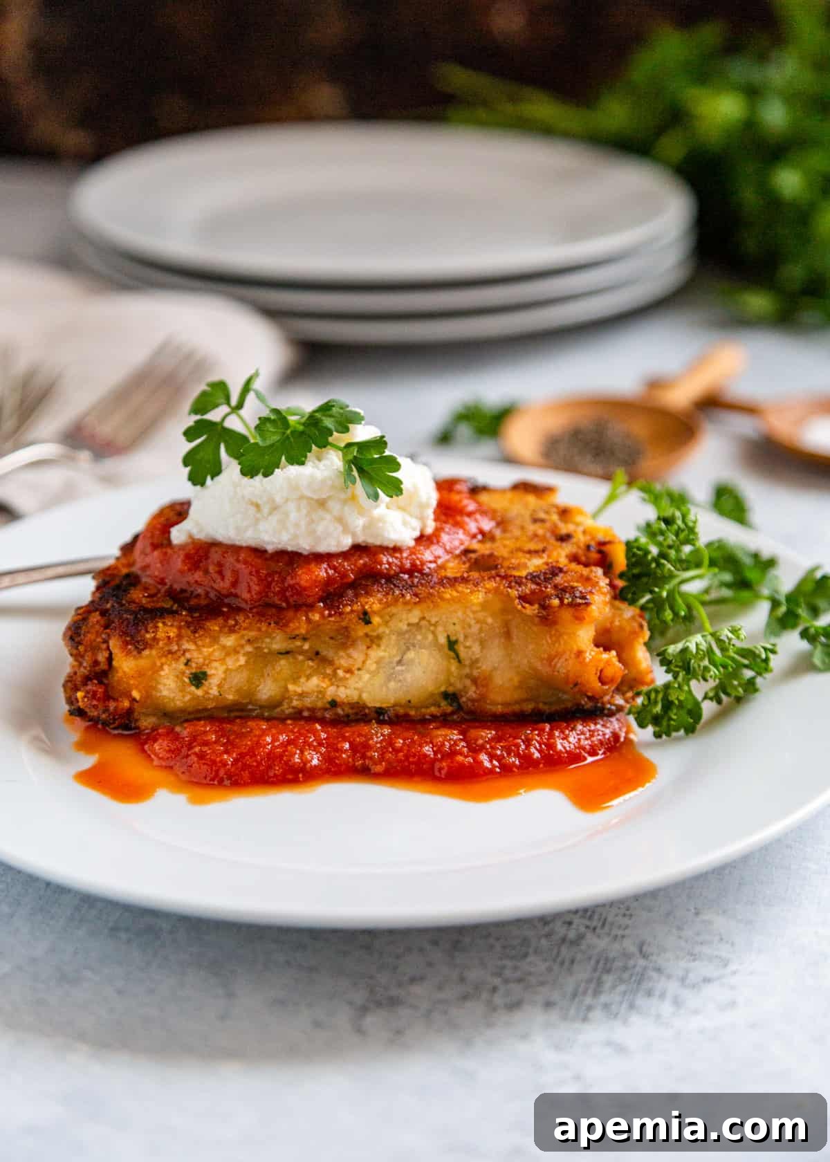 Side view close-up of cheese-crusted baked ziti on a white plate, garnished with ricotta and fresh parsley