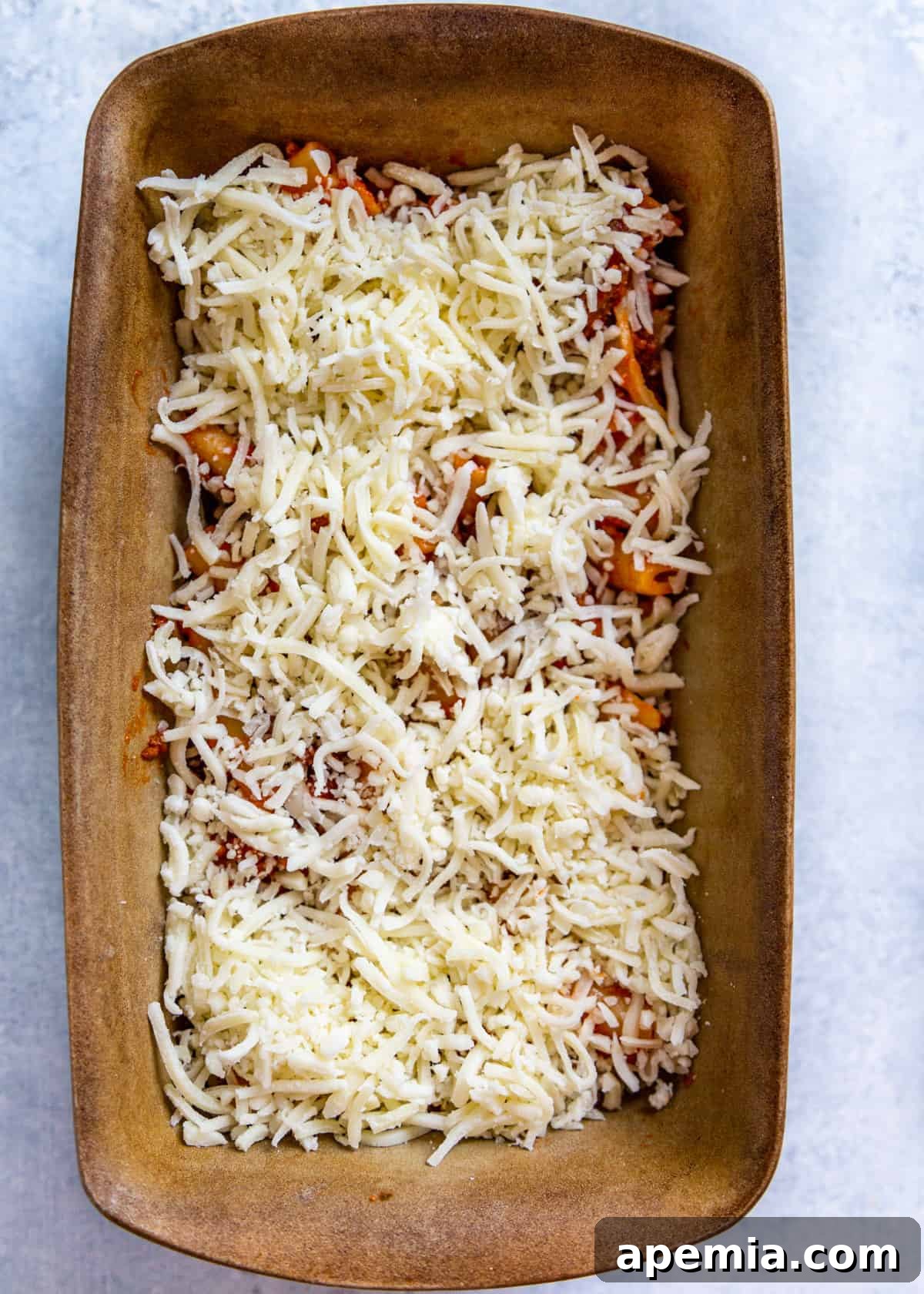 Overhead view of ziti pasta and sauce covered in a generous layer of cheese in a baking dish, ready for baking