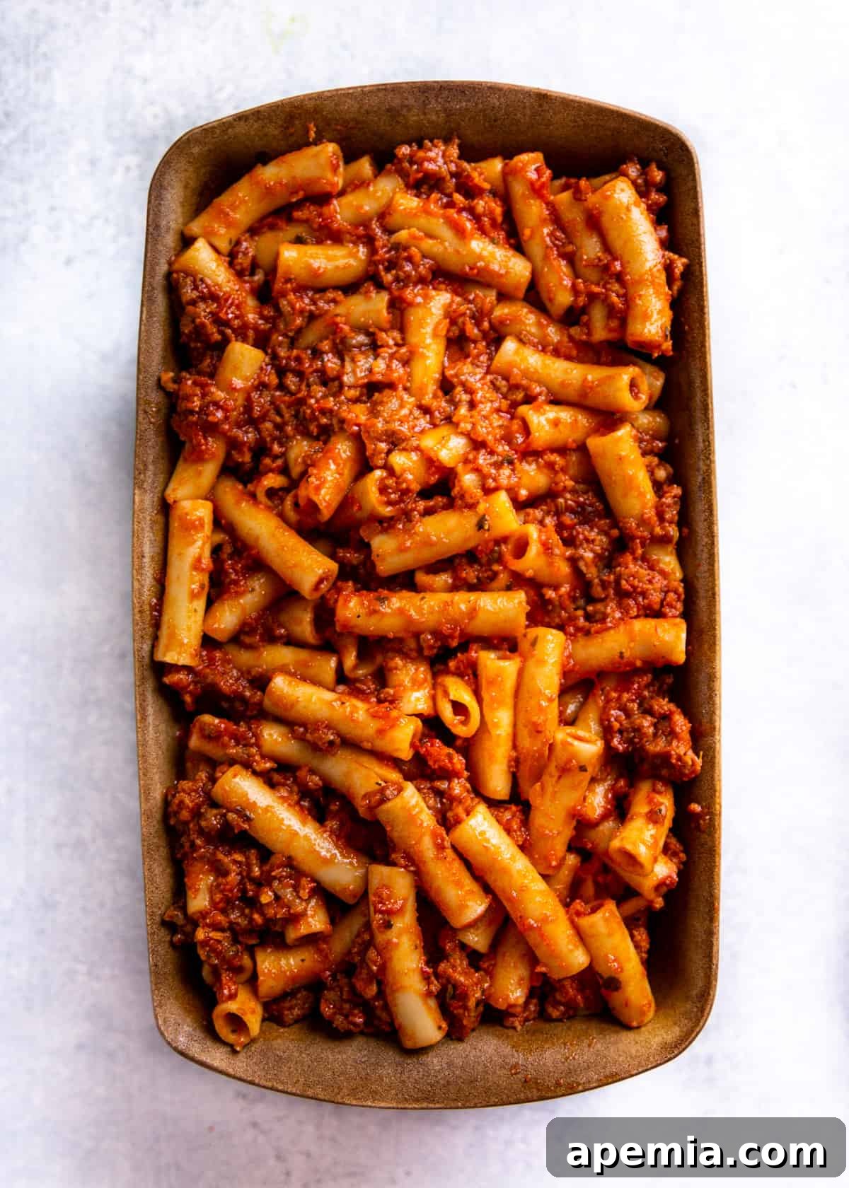 Overhead view of ziti, sauce, and cheese, with more pasta and sauce visible in a large baking dish