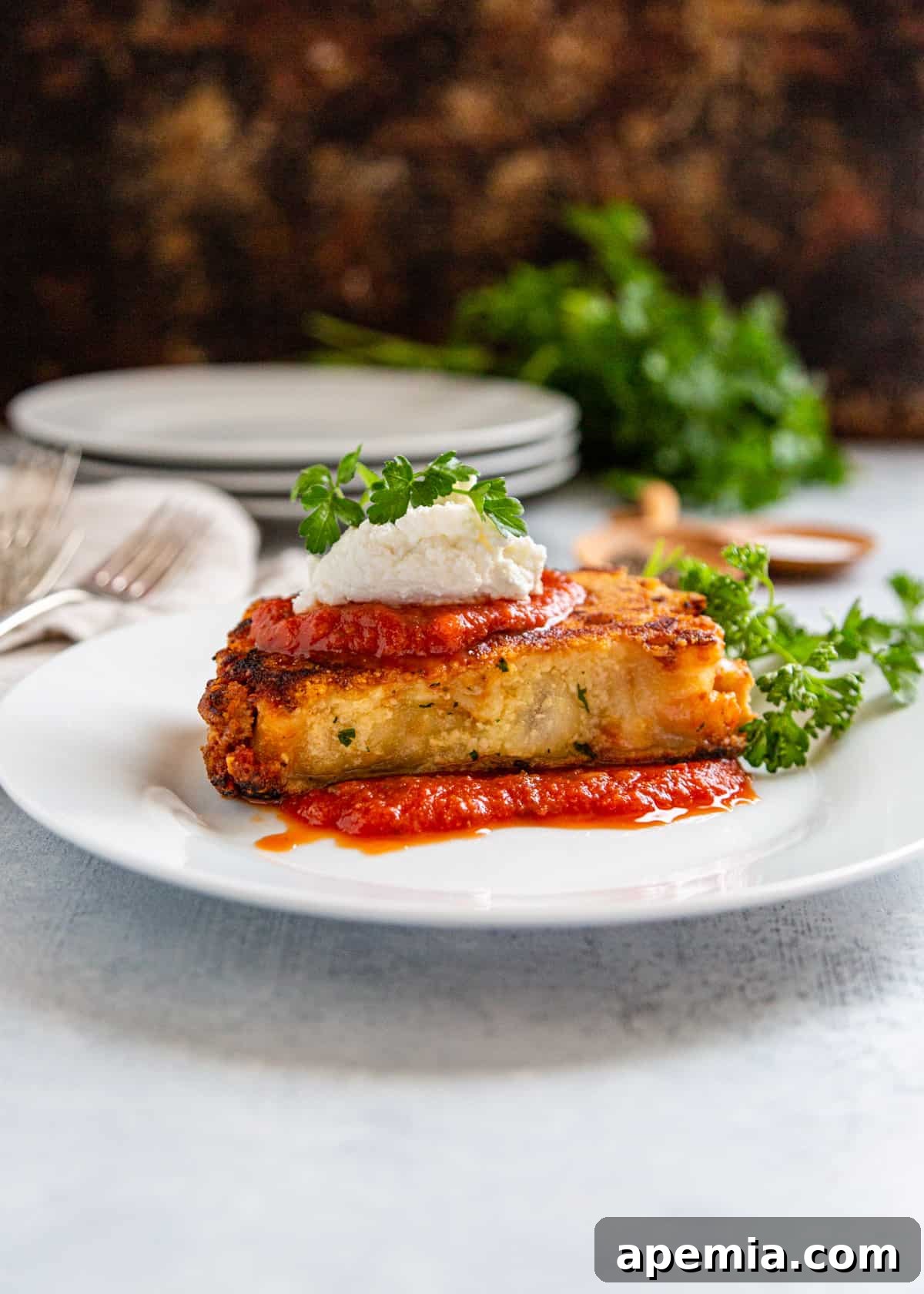 Side view of cheese-crusted baked ziti on a white plate, topped with ricotta and fresh parsley