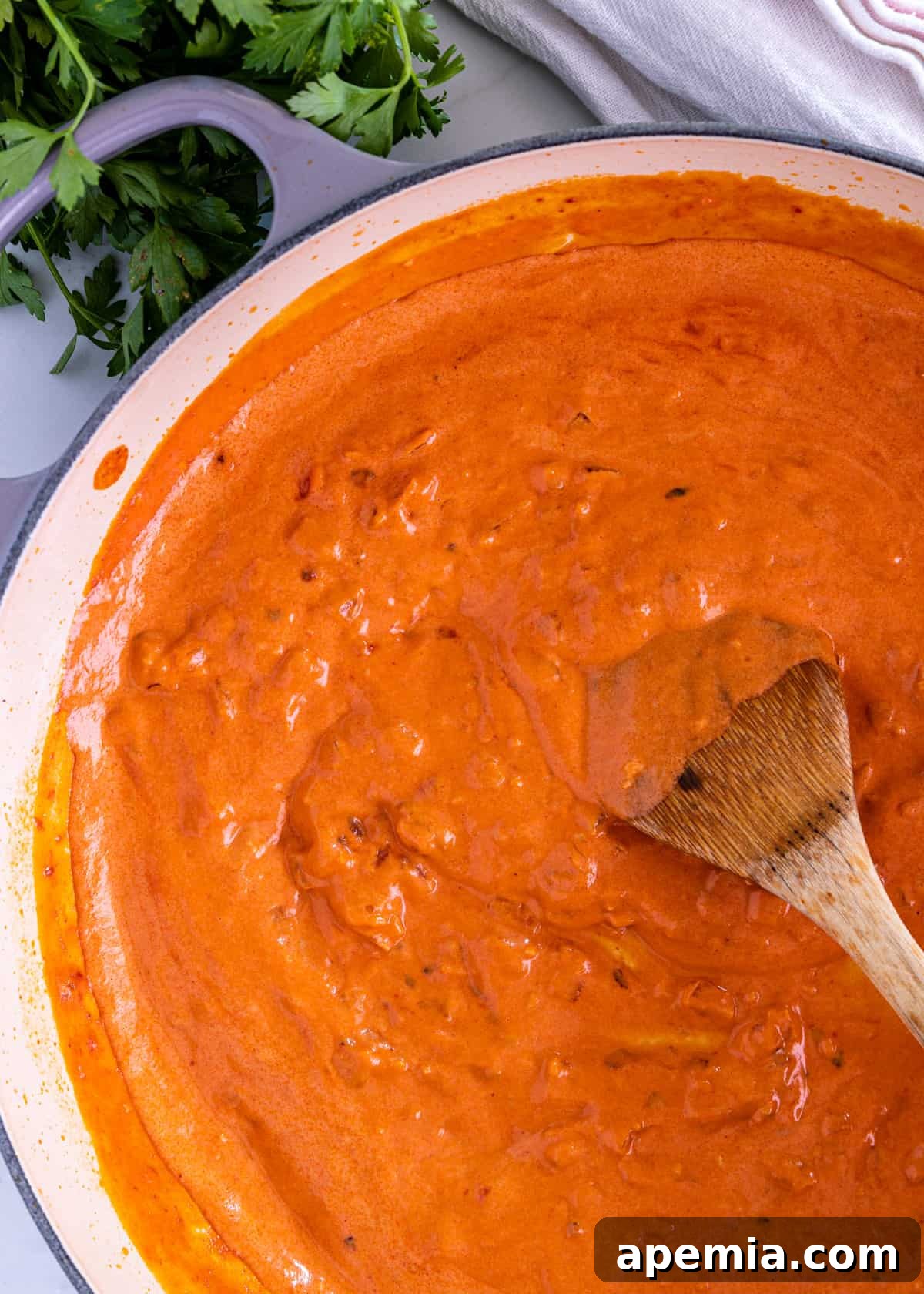 Overhead shot of a wooden spoon stirring a large pot of simmering vodka sauce, showcasing its rich orange color and creamy texture.