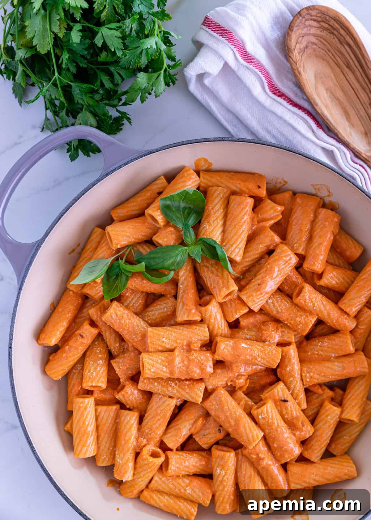 Overhead view of rigatoni pasta mixed with creamy vodka sauce, garnished with fresh basil leaves, resting in a large pot before serving.