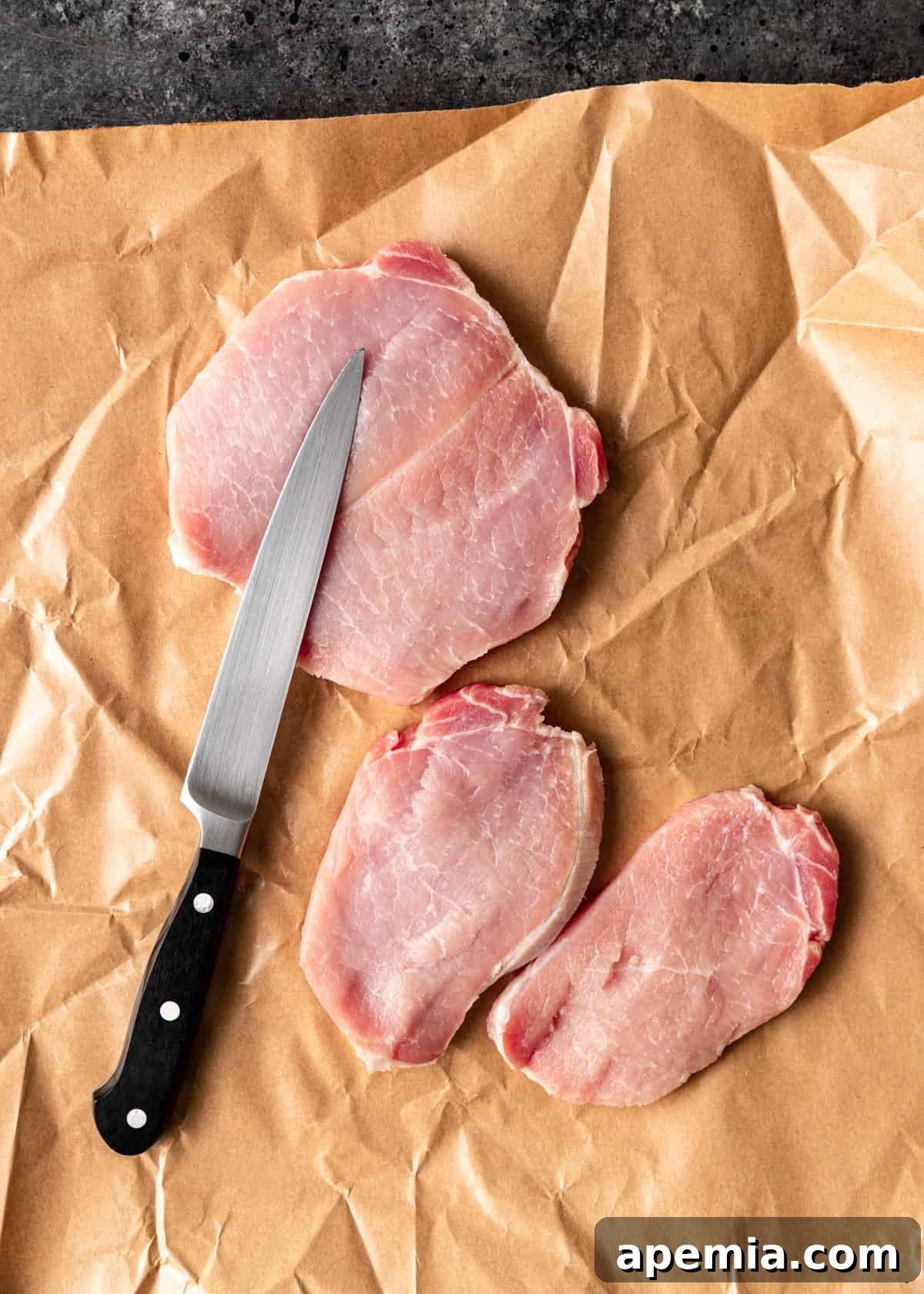 Overhead view showing three butterflied pork chops on butcher paper, resulting in four thinner cutlets, ready for tenderizing and seasoning.
