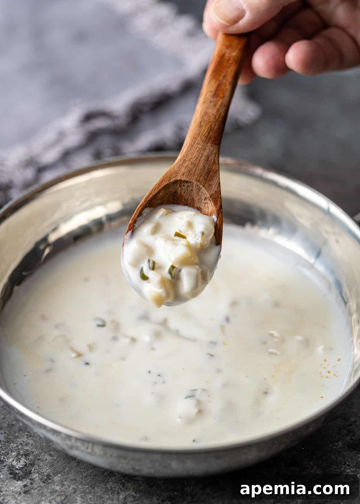 a hand lifting a wooden spoon with pineapple pachadi over a metal dish with more pachadi