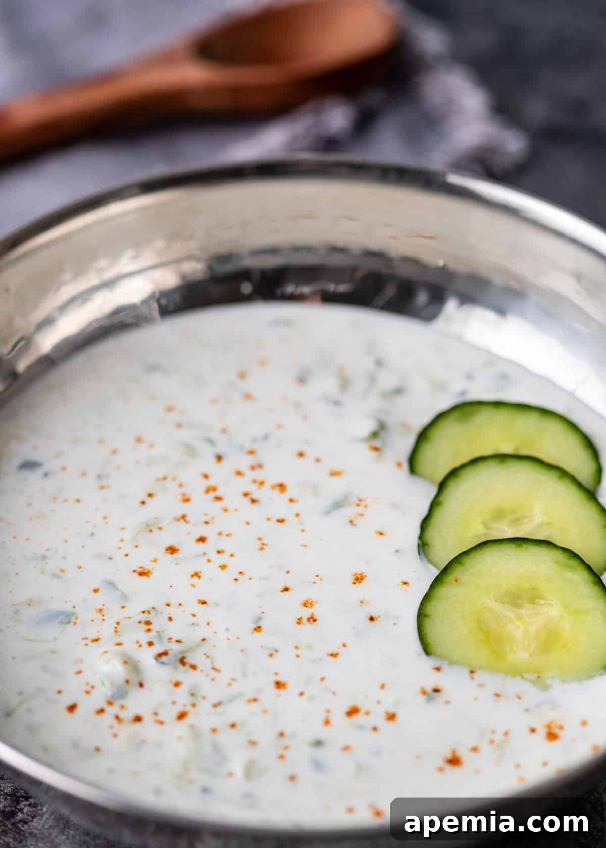 closeup: a silver bowl filled with homemade cucumber raita, featuring finely chopped cucumbers on top for garnish