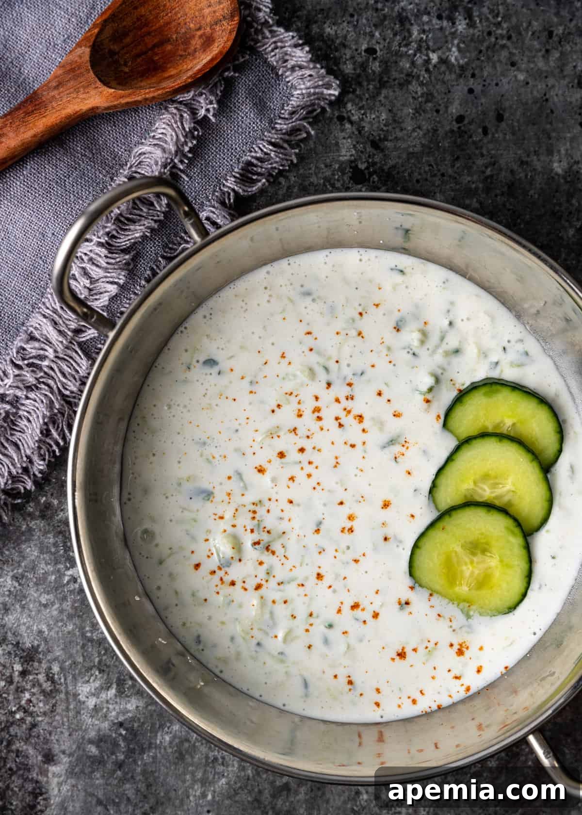 overhead: cucumber raita recipe in a silver bowl with sliced cucumbers on top, elegantly garnished and ready to serve