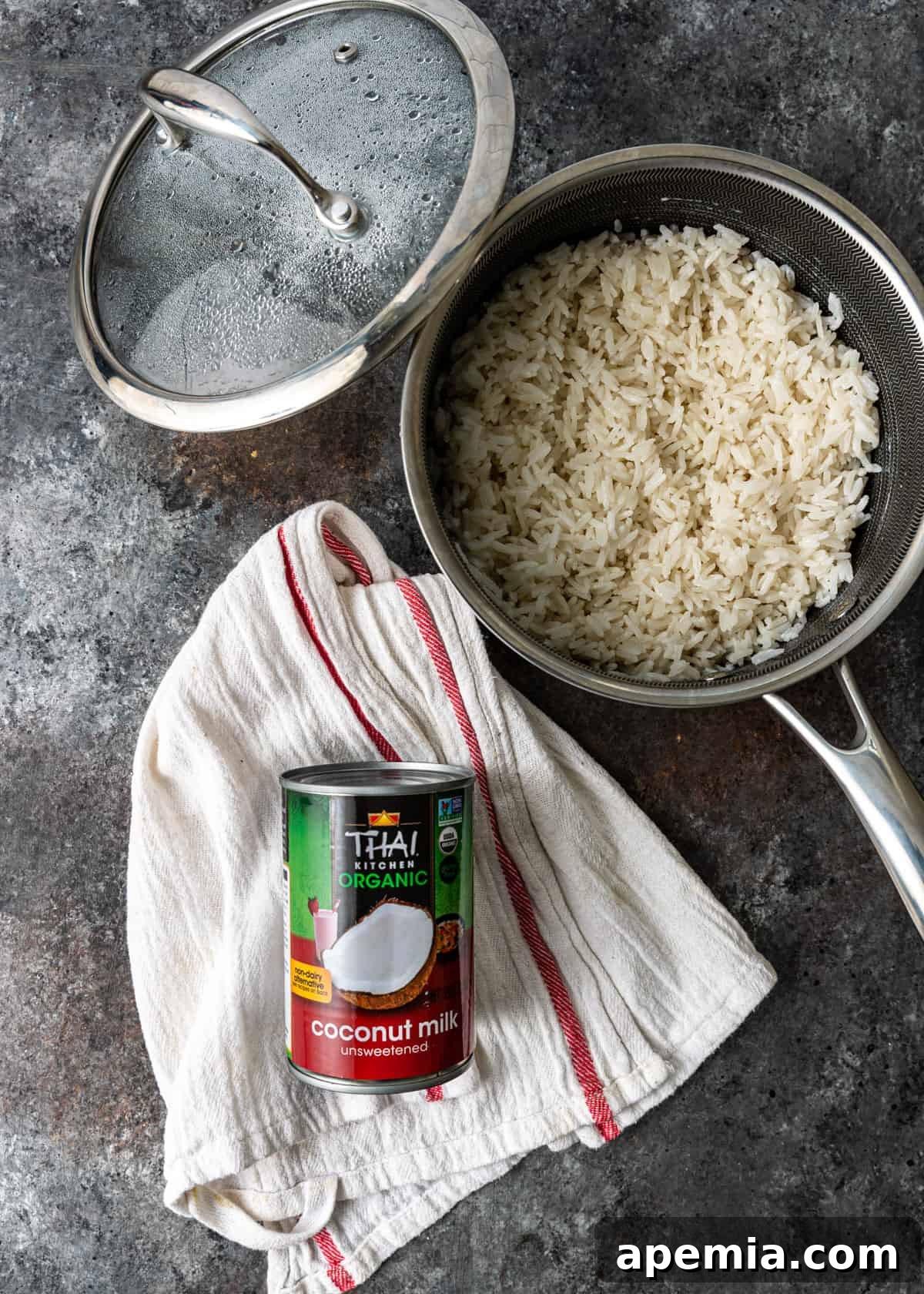 Overhead shot of a pot of cooked rice next to a can of coconut milk, highlighting the base ingredient
