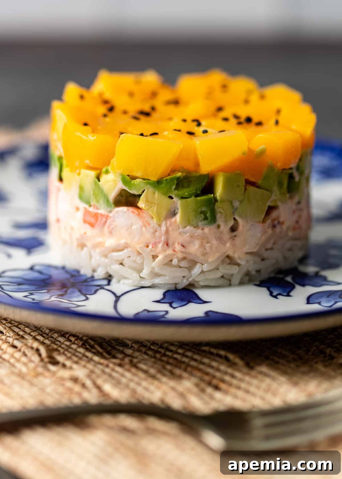 Close-up of a single mango shrimp sushi stack, showing the distinct layers of rice, shrimp, avocado, and mango