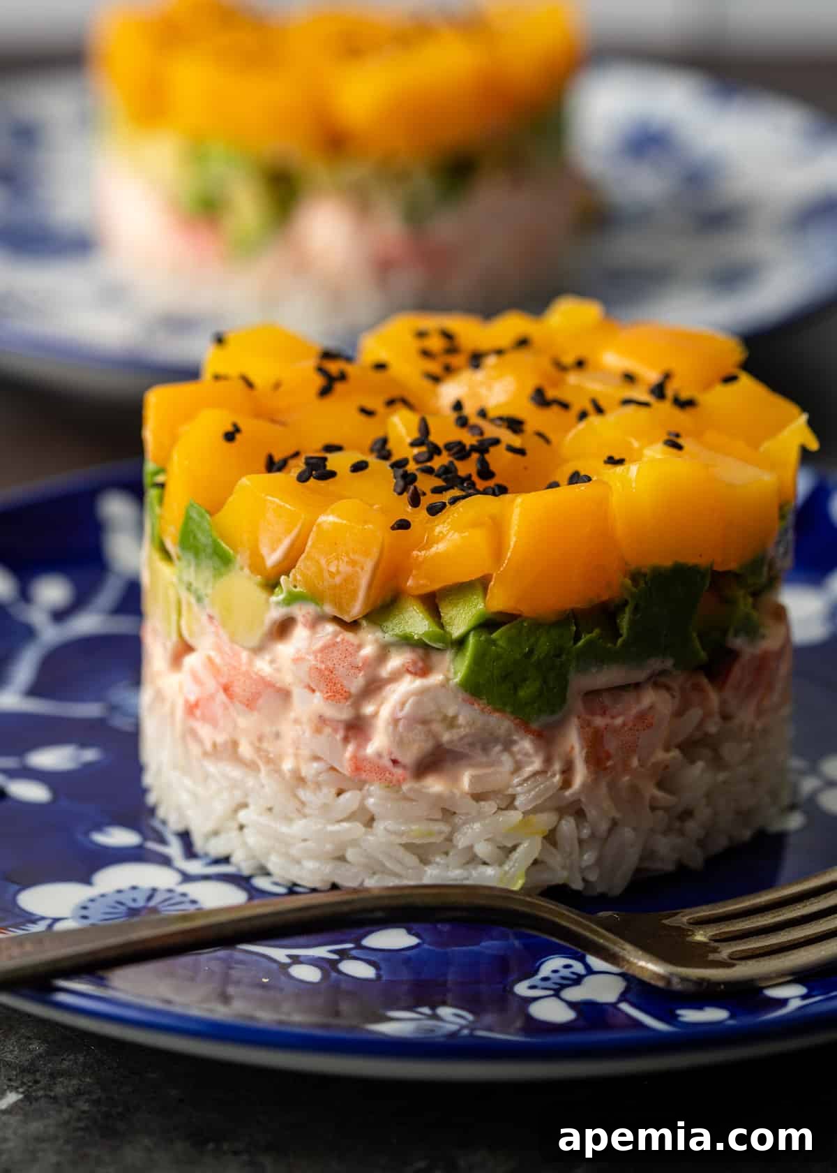 A row of beautifully plated mango shrimp sushi stacks, garnished with black sesame seeds