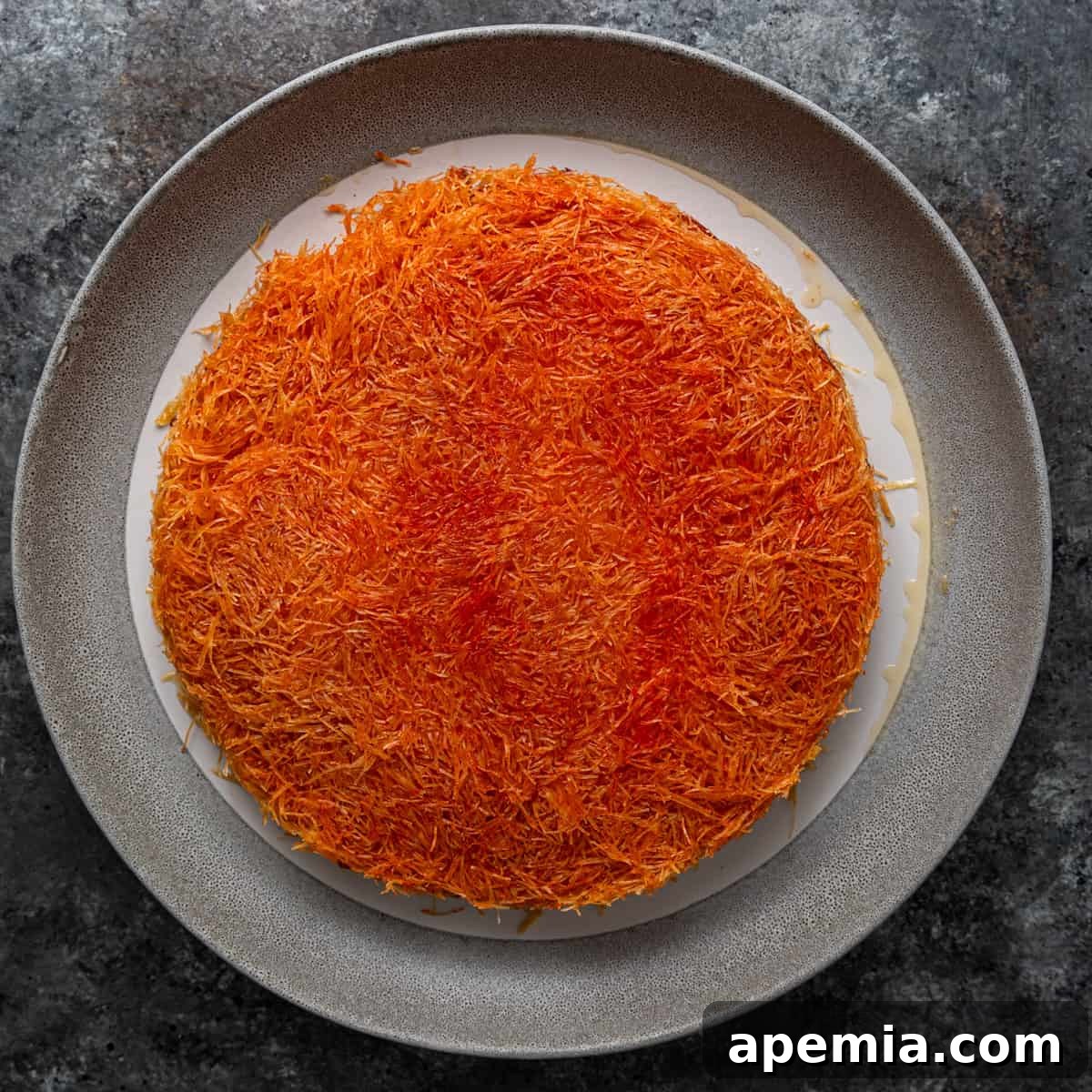 Overhead view of the baking pan being lifted to reveal a perfectly baked knafeh with a visible orange-colored layer.