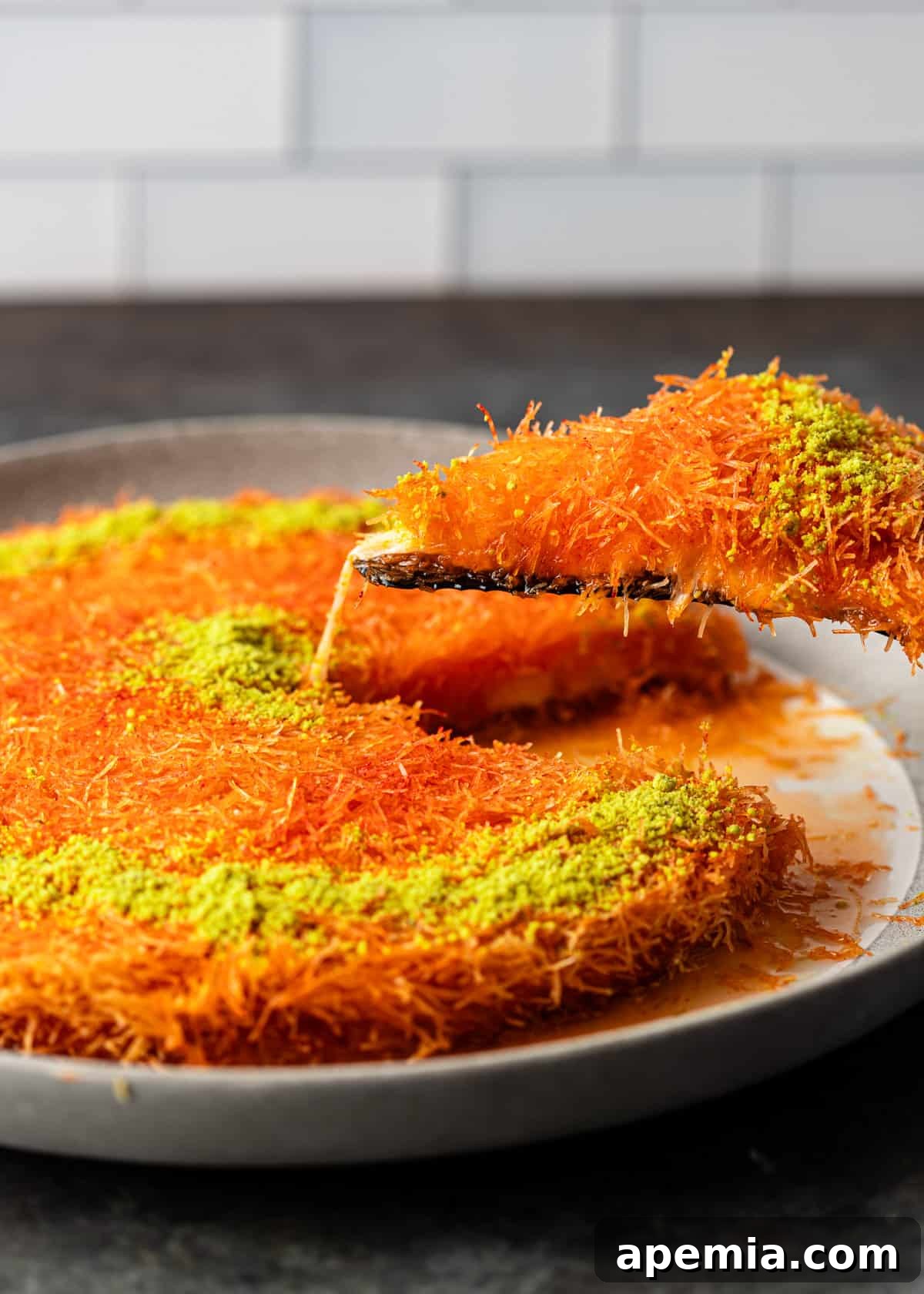 Lifting a slice of knafeh out of a serving dish, highlighting its crisp texture and melted cheese.