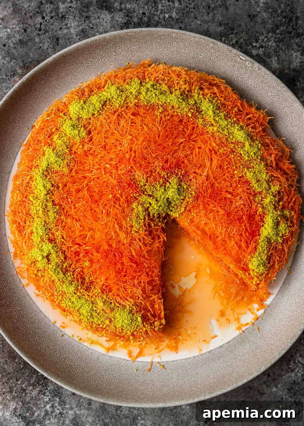 Overhead view of a baked kunafa in a serving dish with a slice already removed, showing the golden crust and cheese.