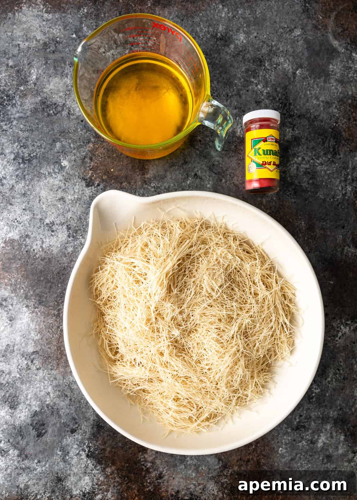 Overhead view of cut filo dough in a bowl, positioned next to a measuring cup filled with golden melted ghee.