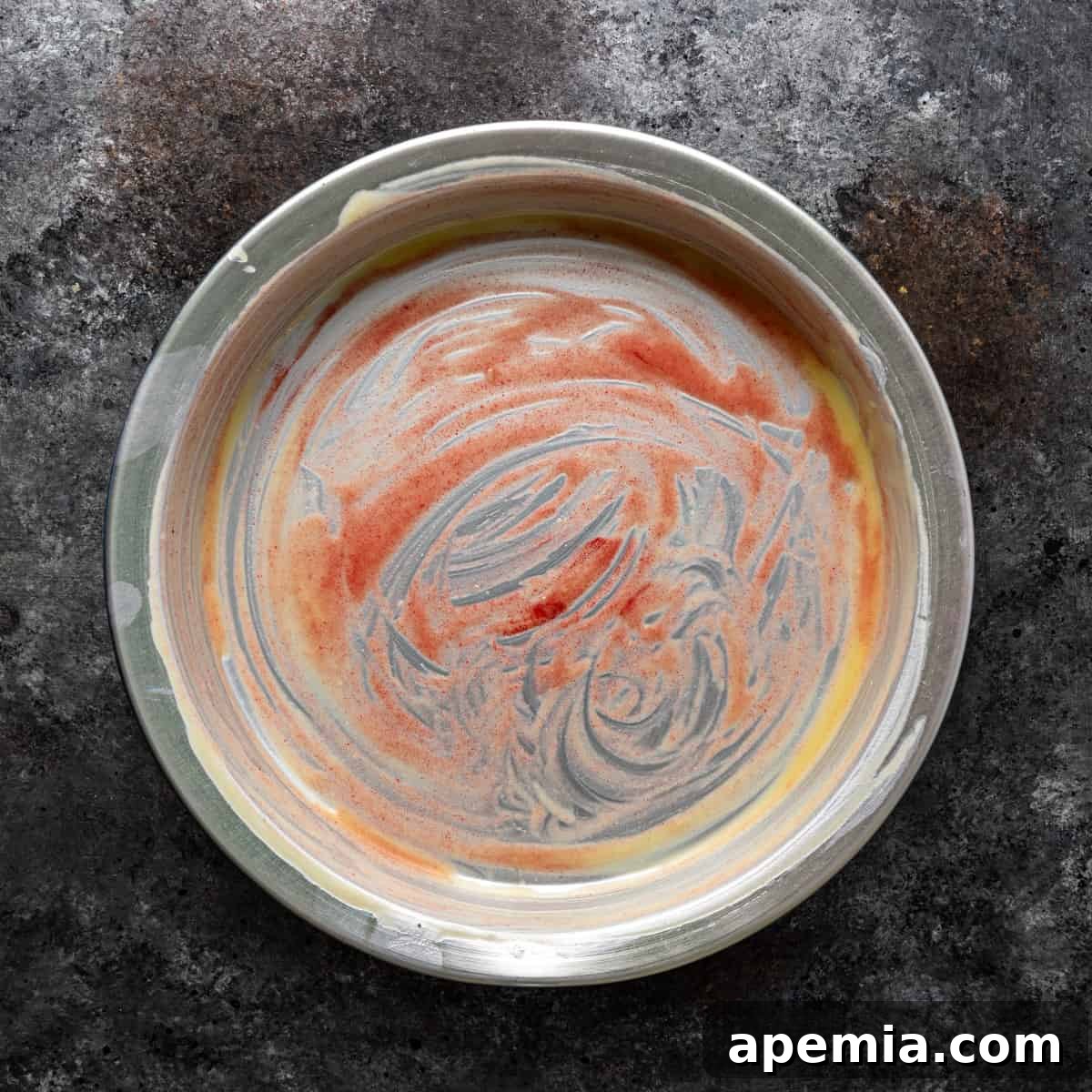 Overhead shot of a buttered 9-inch baking pan, lightly colored with pastry coloring, ready for the Knafeh layers.