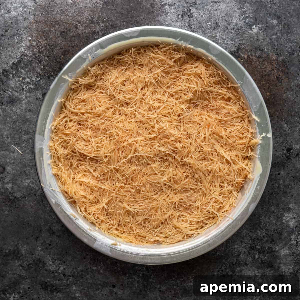 Overhead view of the first uniform layer of shredded filo dough (kataifi) pressed into a 9-inch baking pan.