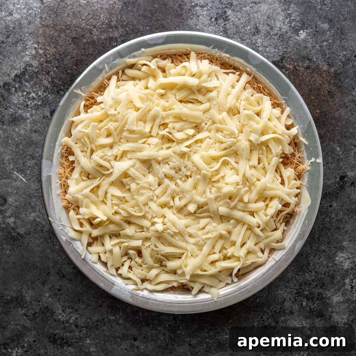 Overhead view of a generous layer of shredded cheese spread evenly on top of the first layer of filo dough in a 9-inch pan.