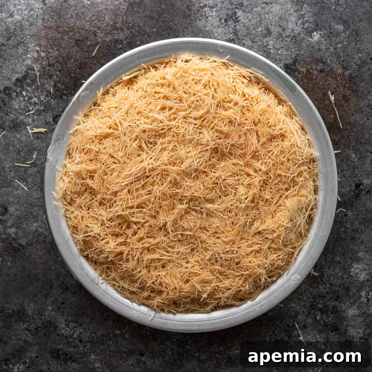 Overhead view of the top layer of shredded filo dough evenly distributed over the cheese in a 9-inch pan, ready for baking.
