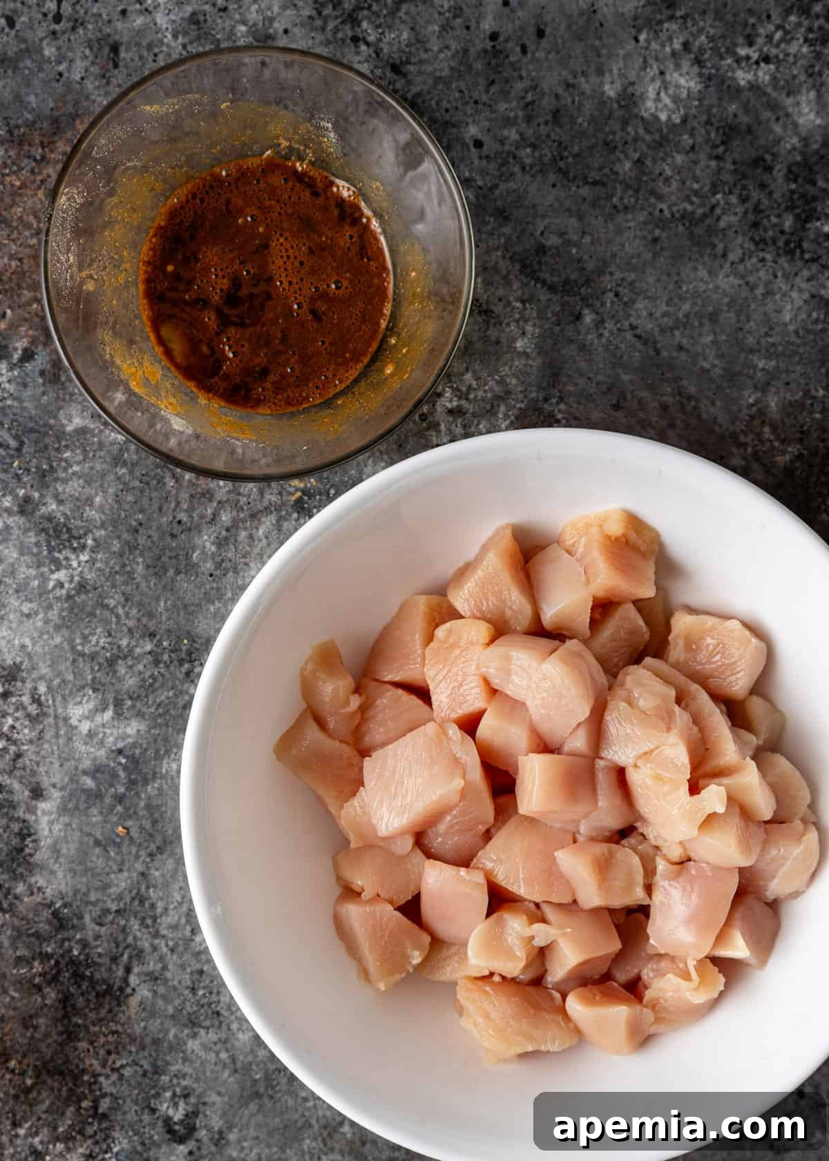 overhead: cubed raw chicken with a bowl of sauce