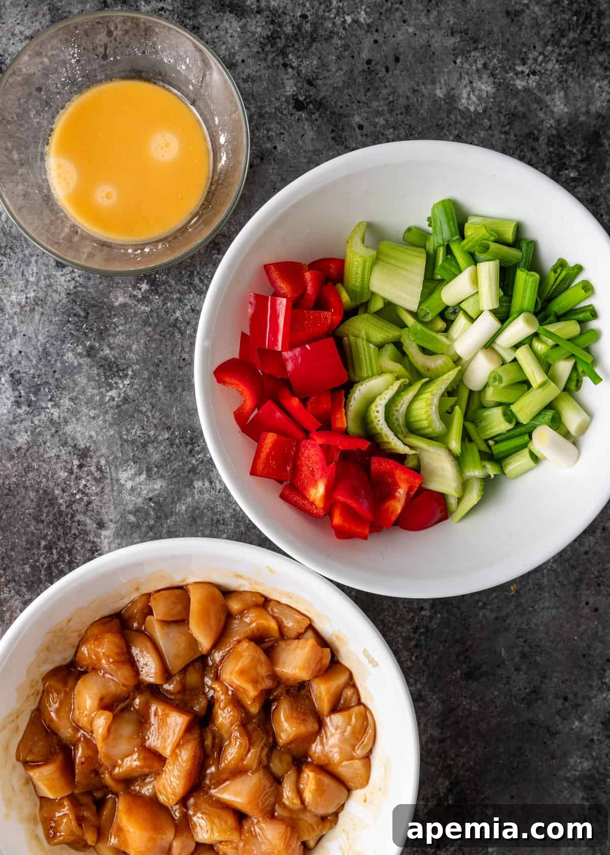 overhead: marinated cubed raw chicken with a bowl of chopped veggies and a small bowl of sauce