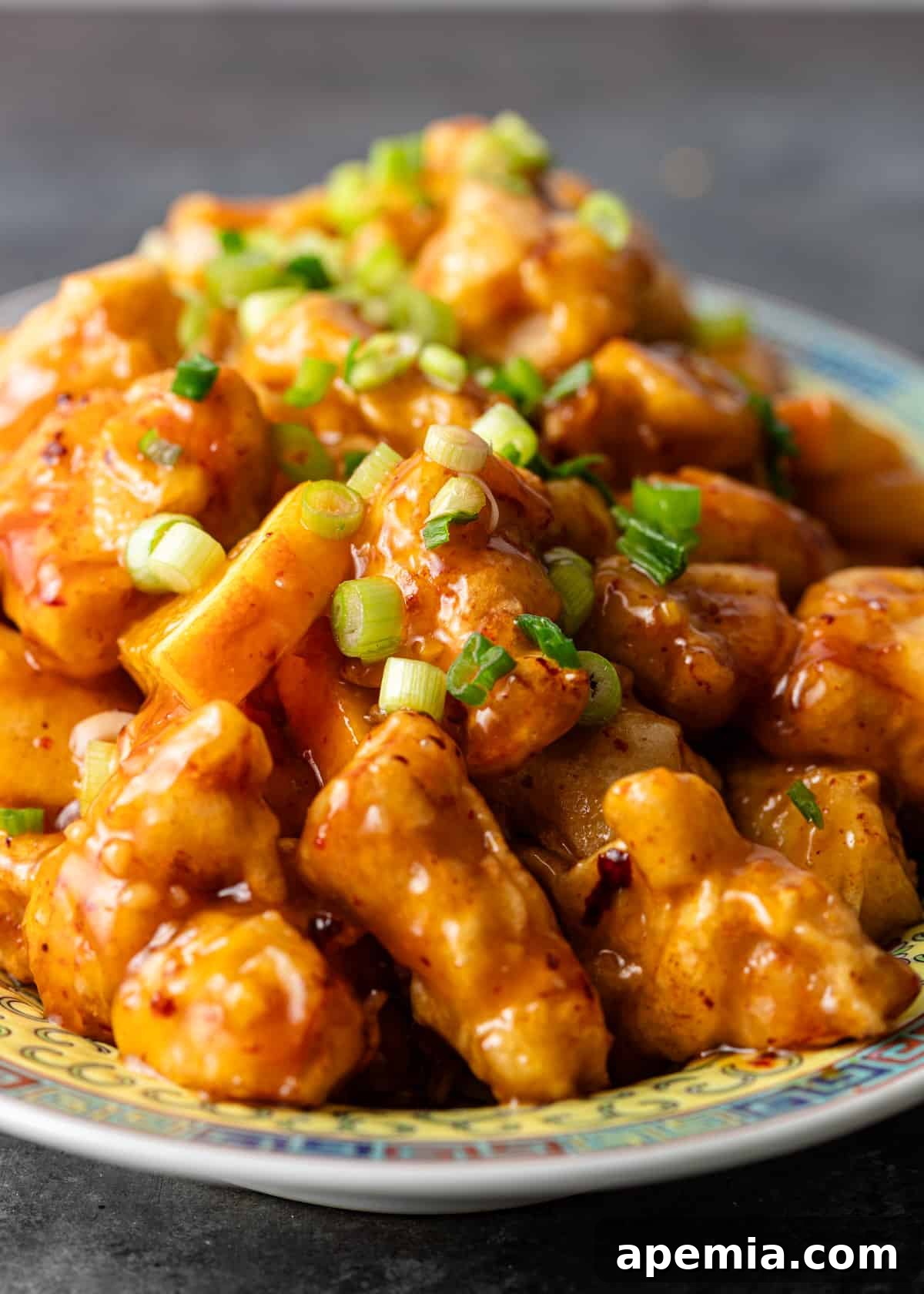Close-up of a generous serving of crispy orange chicken, coated in sticky sauce and adorned with bright green onions, ready to be enjoyed.