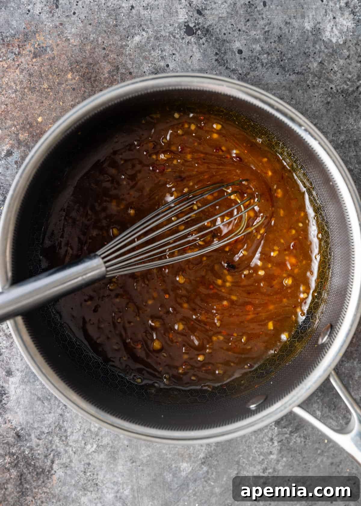 Overhead view of a rich orange sauce being whisked in a large metal bowl, showing its glossy texture and vibrant color.