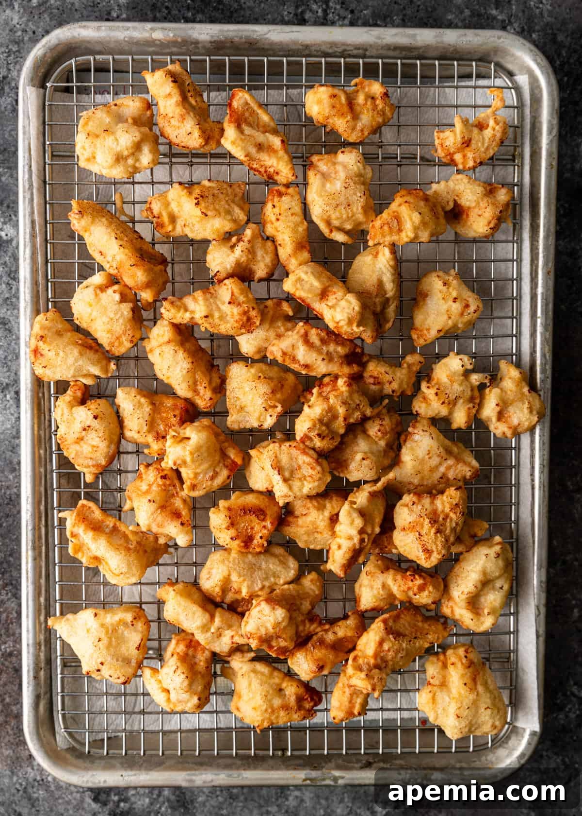 Overhead view of perfectly crispy fried chicken pieces cooling on a wire rack set over a baking sheet.