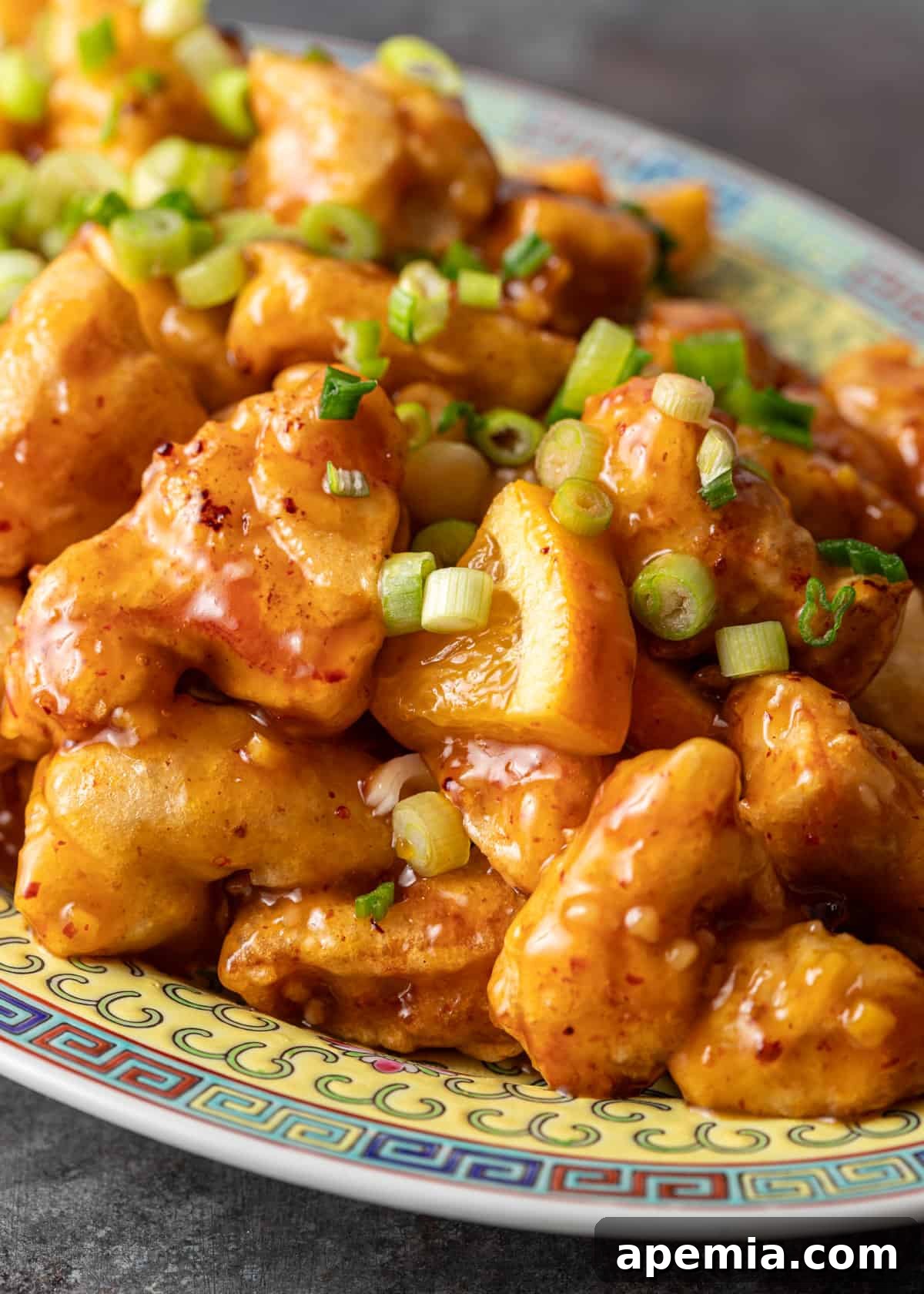 Closeup of the orange chicken recipe, highlighting the glistening sticky sauce, vibrant green onion, and fresh orange wedges for garnish.
