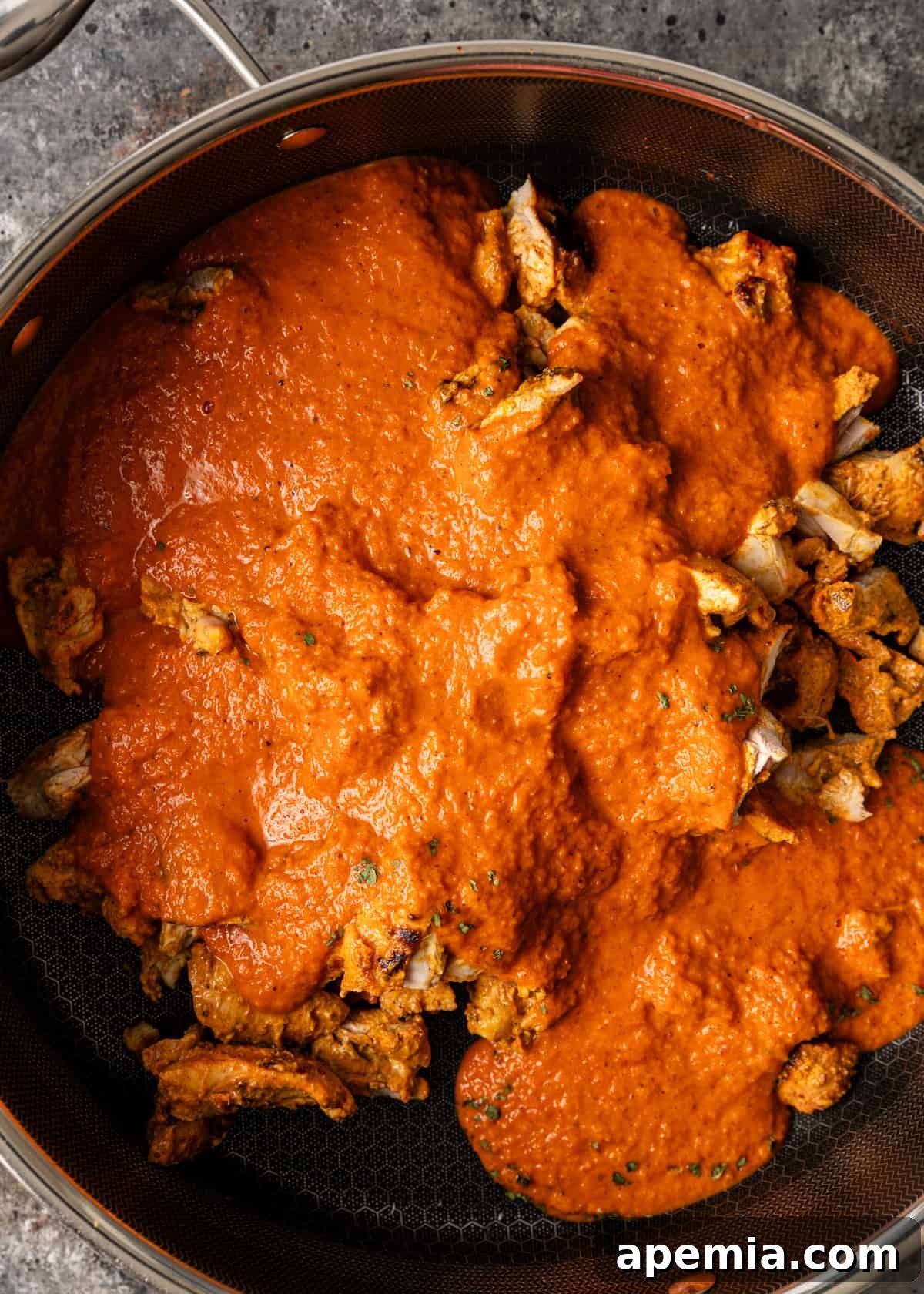 overhead process shot: simmering chicken in masala sauce in a pot
