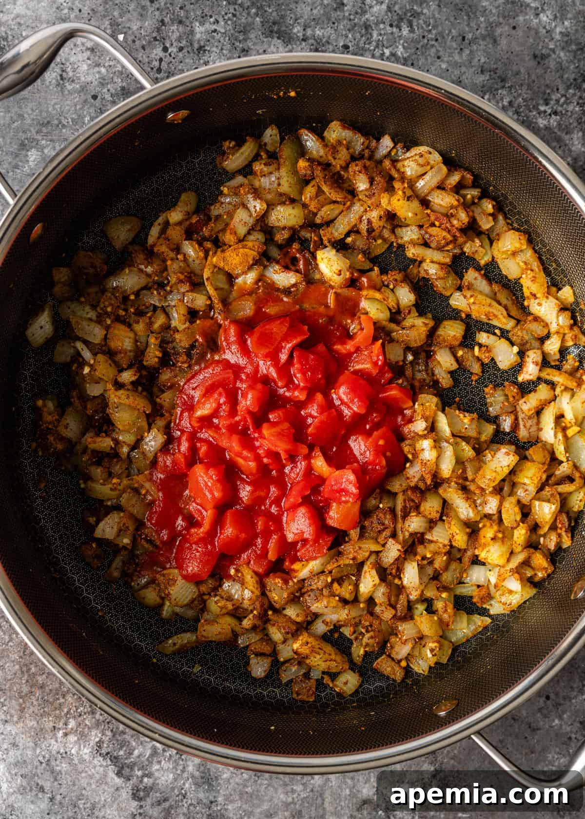 overhead process shot: adding tomatoes to onion, garlic, and ginger in a pot