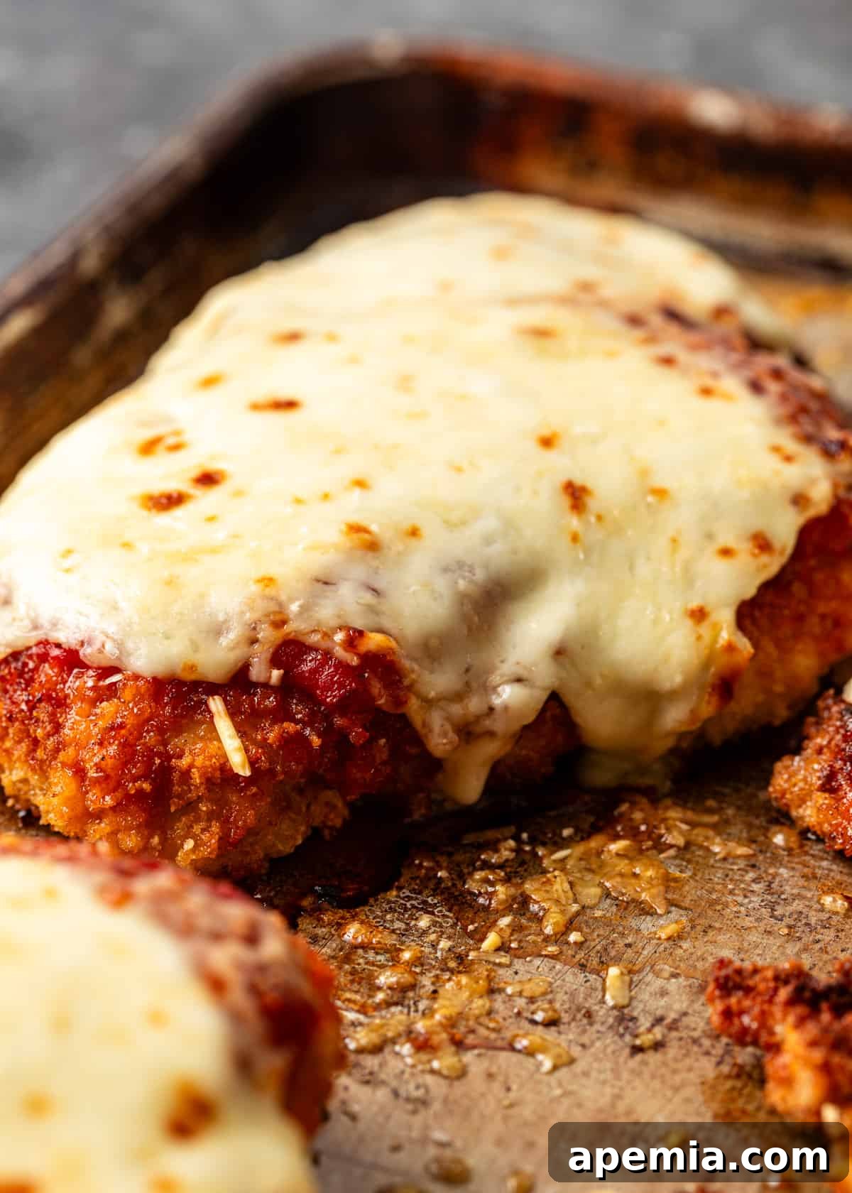 closeup: baked chicken parmigiana on a baking sheet covered in melted cheese