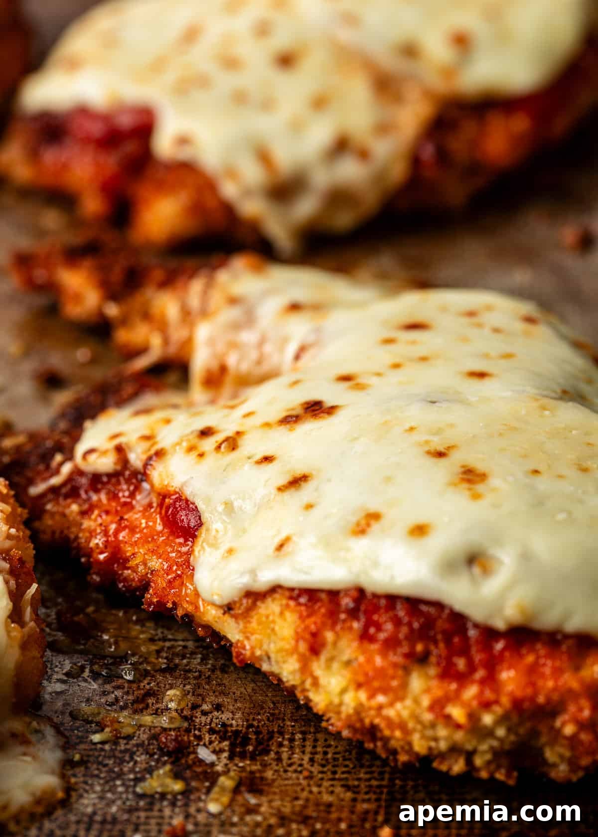 extreme closeup: baked chicken parmigiana on a baking sheet covered in melted cheese