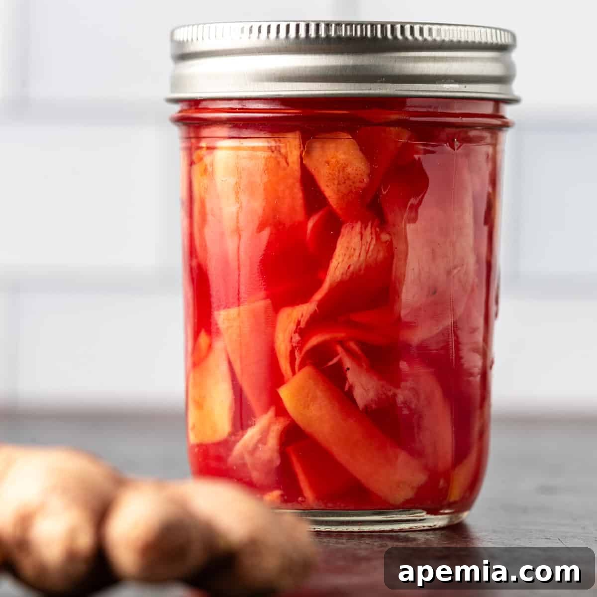Closeup of homemade pickled ginger in a clear glass jar with a lid, showcasing its vibrant pink color and delicate slices.
