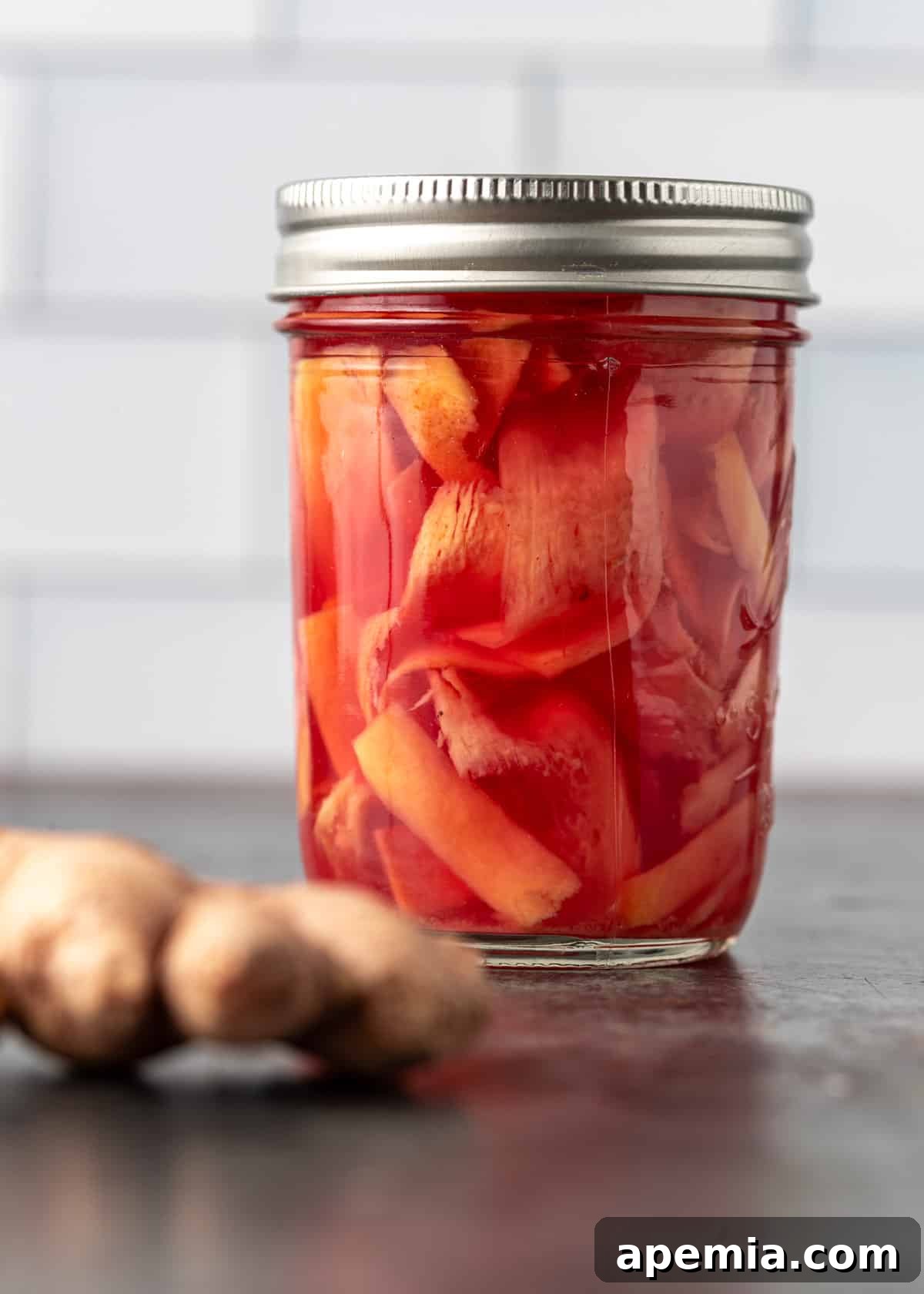 Overhead view of a glass jar filled with homemade pickled ginger, with some slices arranged decoratively around it.