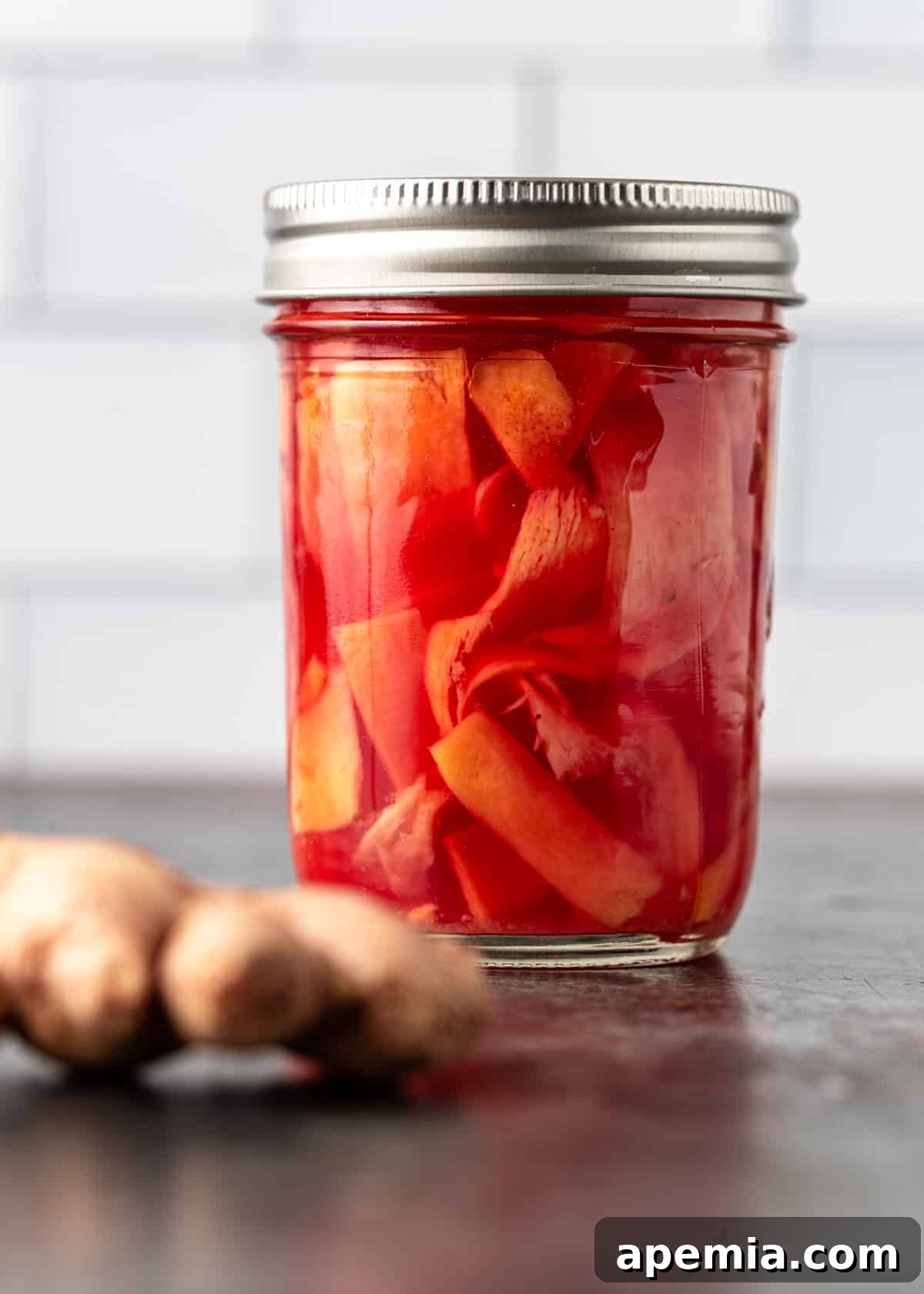 A glass jar of freshly made pickled ginger with the lid on, sitting on a wooden surface, ready for refrigeration.