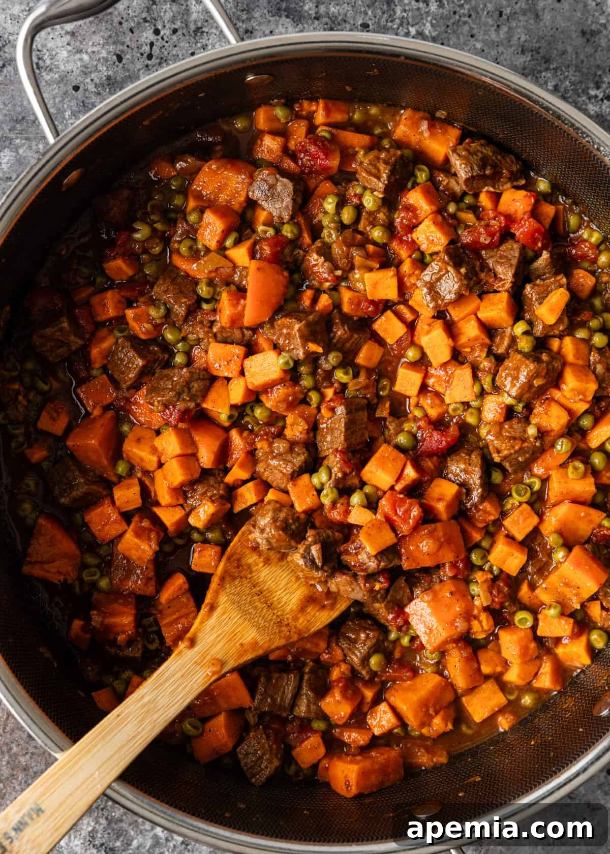 Spiced Beef and Sweet Potato Tagine 7 A wooden spoon stirring beef tagine, rich with broth and spices, as it simmers in a deep frying pan, illustrating the slow cooking process.