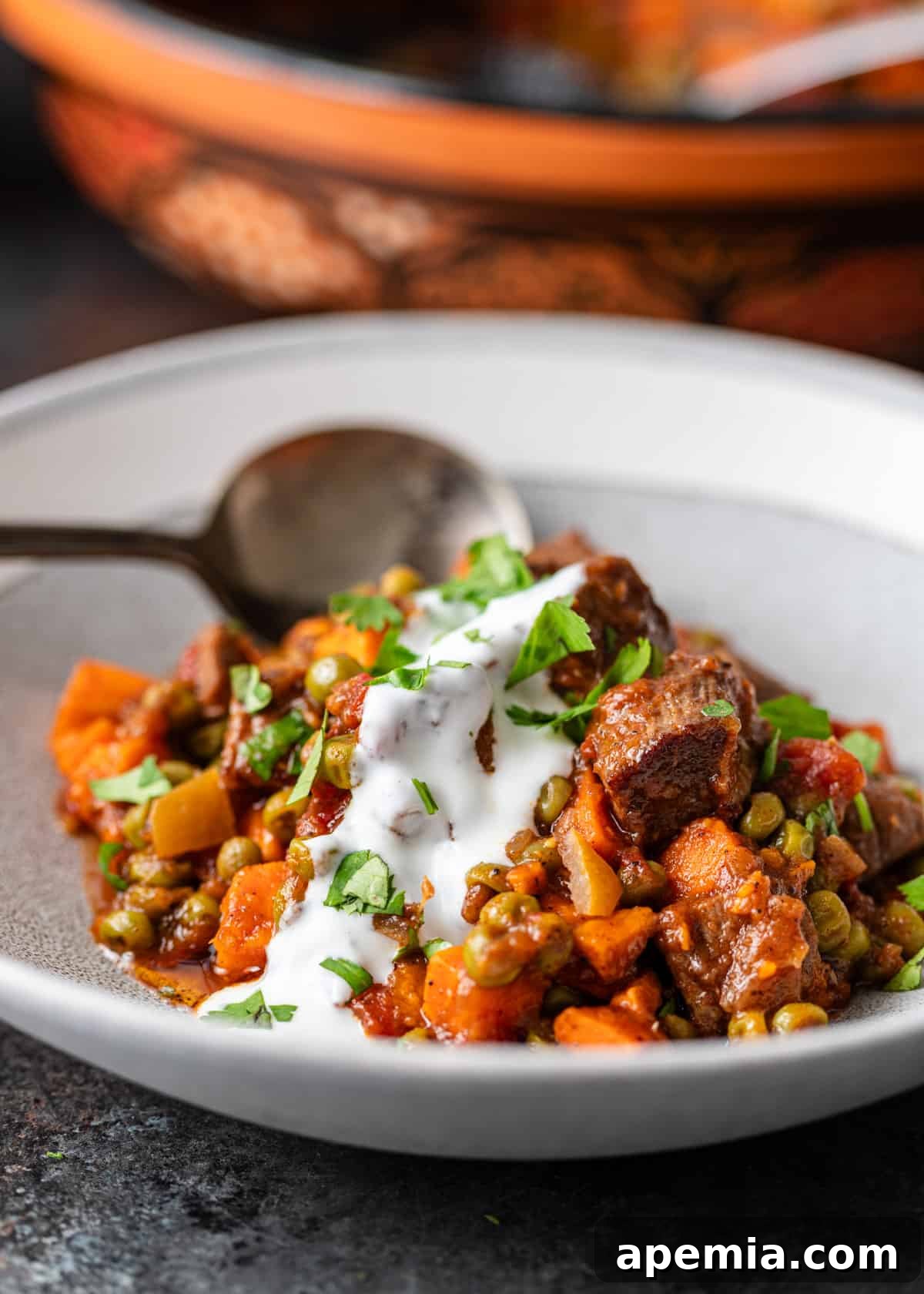 Spiced Beef and Sweet Potato Tagine 10 Side view of a serving of beef tagine with sweet potatoes, elegantly presented in a white dish, topped with a creamy white sauce and fresh green herbs.