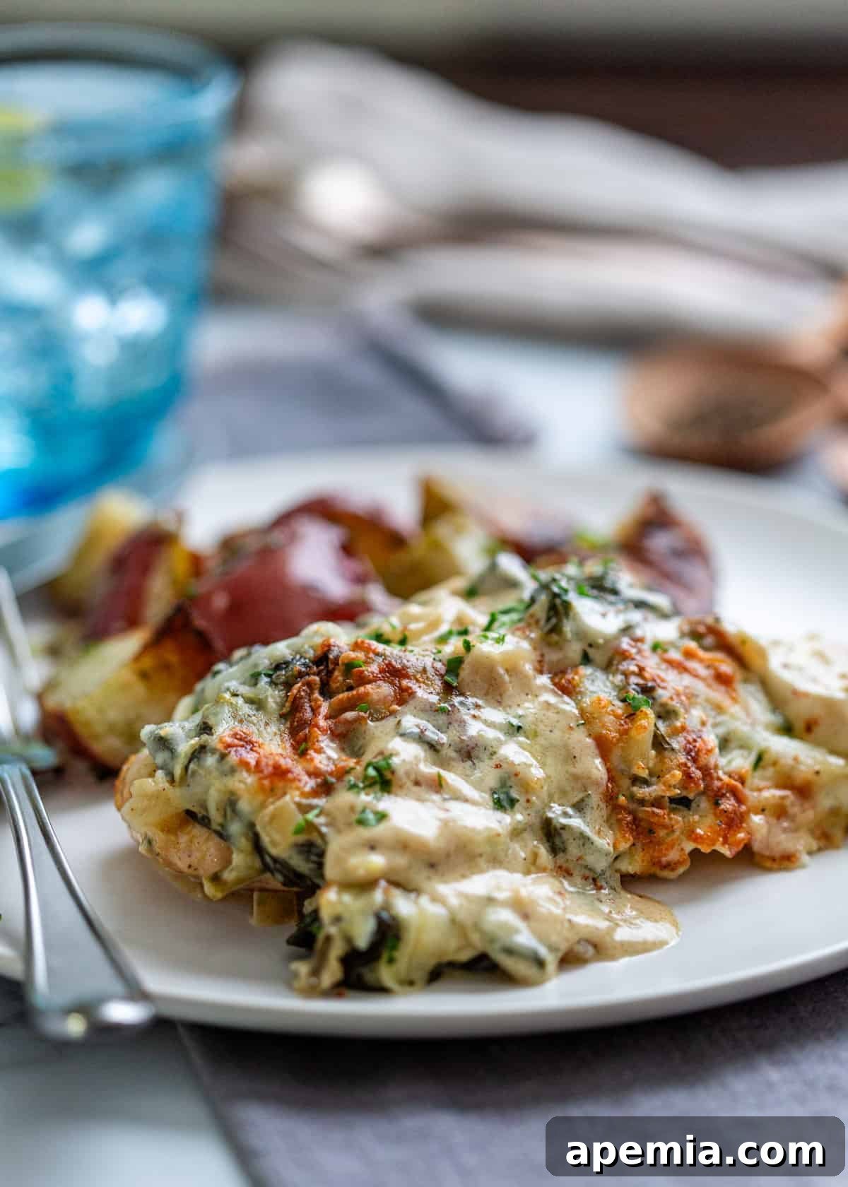 side view: a piece of chicken florentine on a white plate with a fork and roasted potatoes