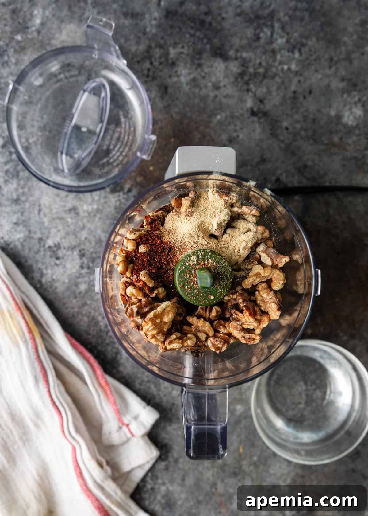 overhead process shot: walnuts, Aleppo pepper, coriander, fenugreek, cayenne, black pepper, & saffron in blender and ½ cup warm water in measuring cup off to side