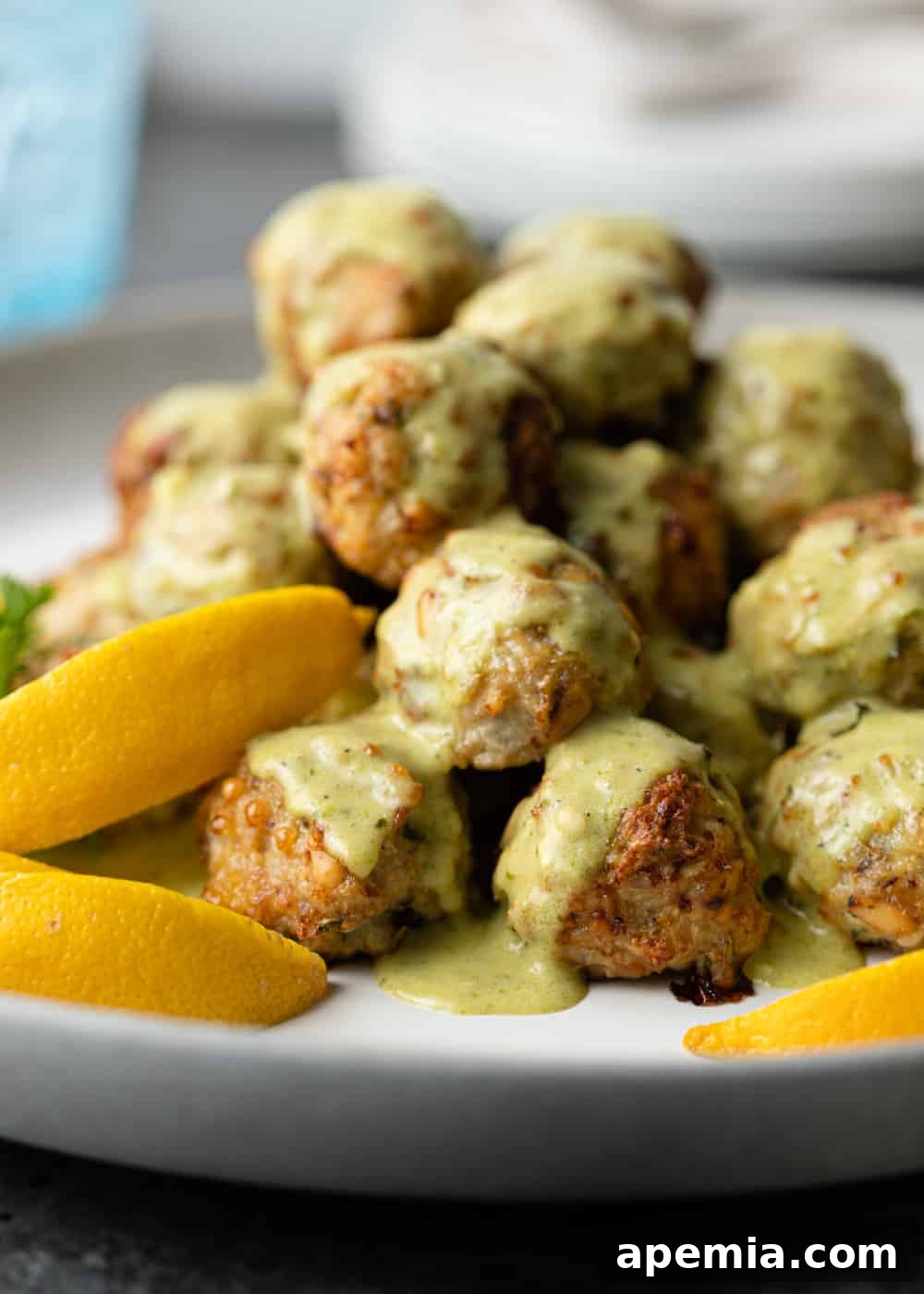 Close-up of the delicious chicken meatball recipe served on a plate with creamy Alfredo sauce and garnished with fresh lemon wedges.