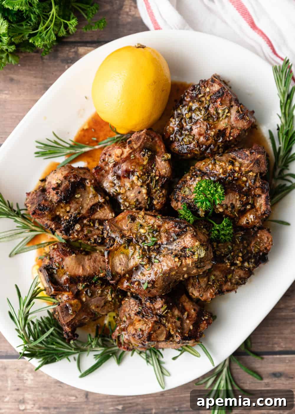 overhead: greek lamb chops on a serving patter with herbs and lemon on the side, highlighting the fresh ingredients