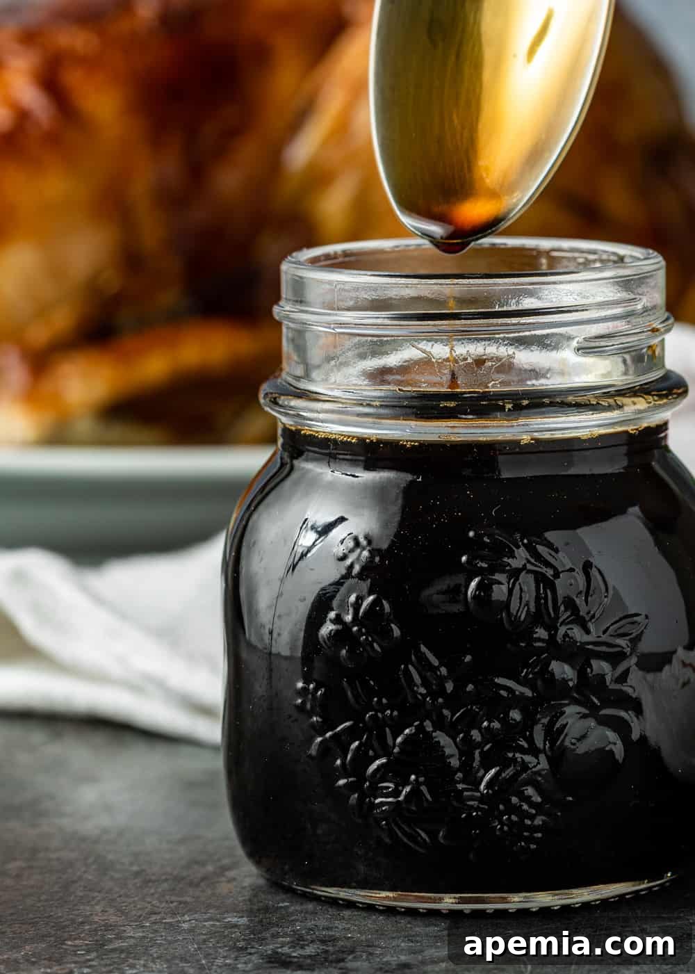 Extreme closeup: lifting a spoon out of a small glass jar of teriyaki sauce, showing its rich, thick texture.