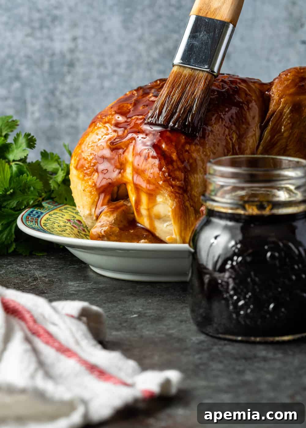 Brushing teriyaki sauce onto a whole roast chicken with a jar full of more sauce visible, showcasing the application.