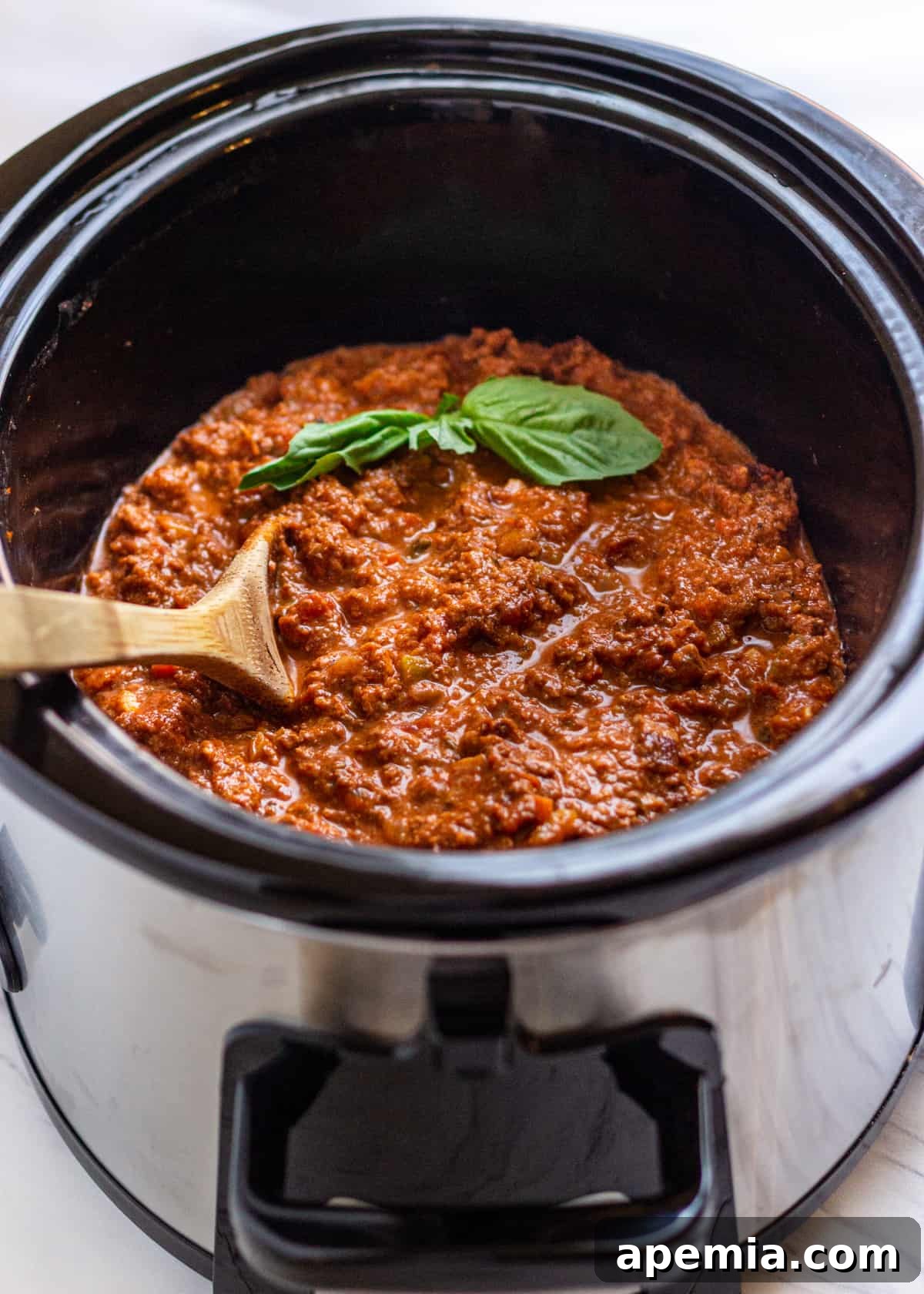 overhead: stirring bolognese sauce in a slow cooker with fresh basil on top