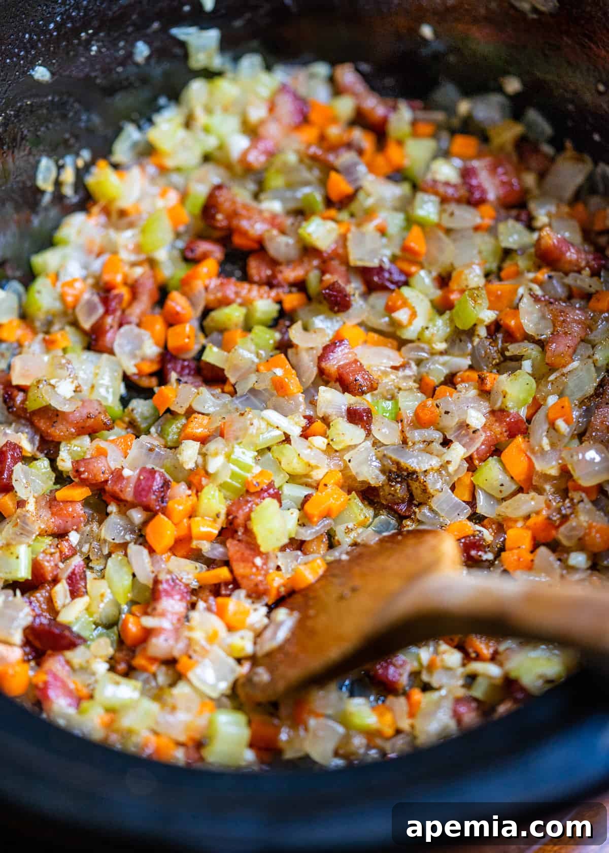 closeup: cooking carrots, onion, celery, and pancetta in a skillet with a wooden spoon stirring