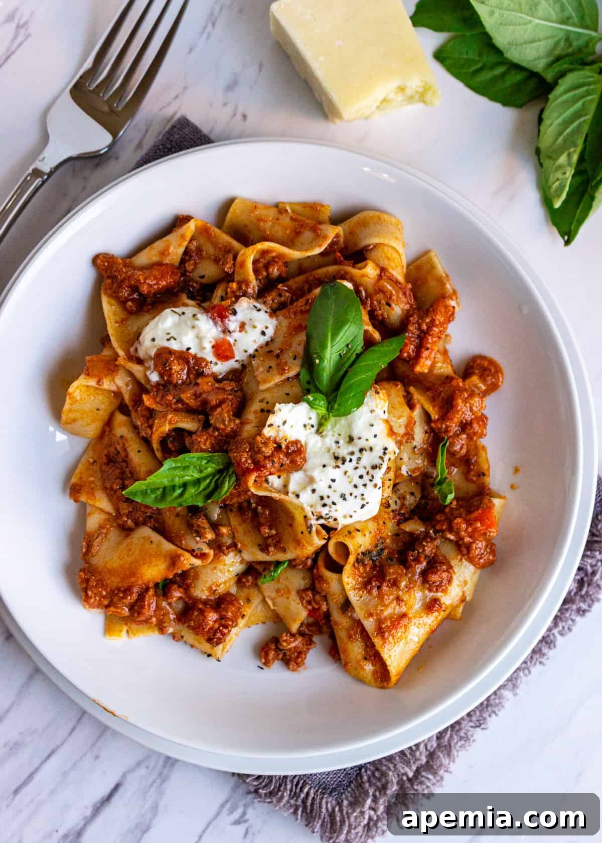 overhead: a plate of tagliatelle bolognese with burrata and fresh basil on top